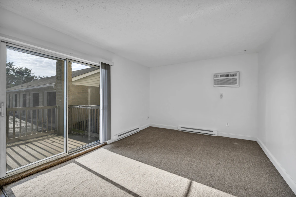 An empty room with brown carpet and a sliding glass door to a deck
