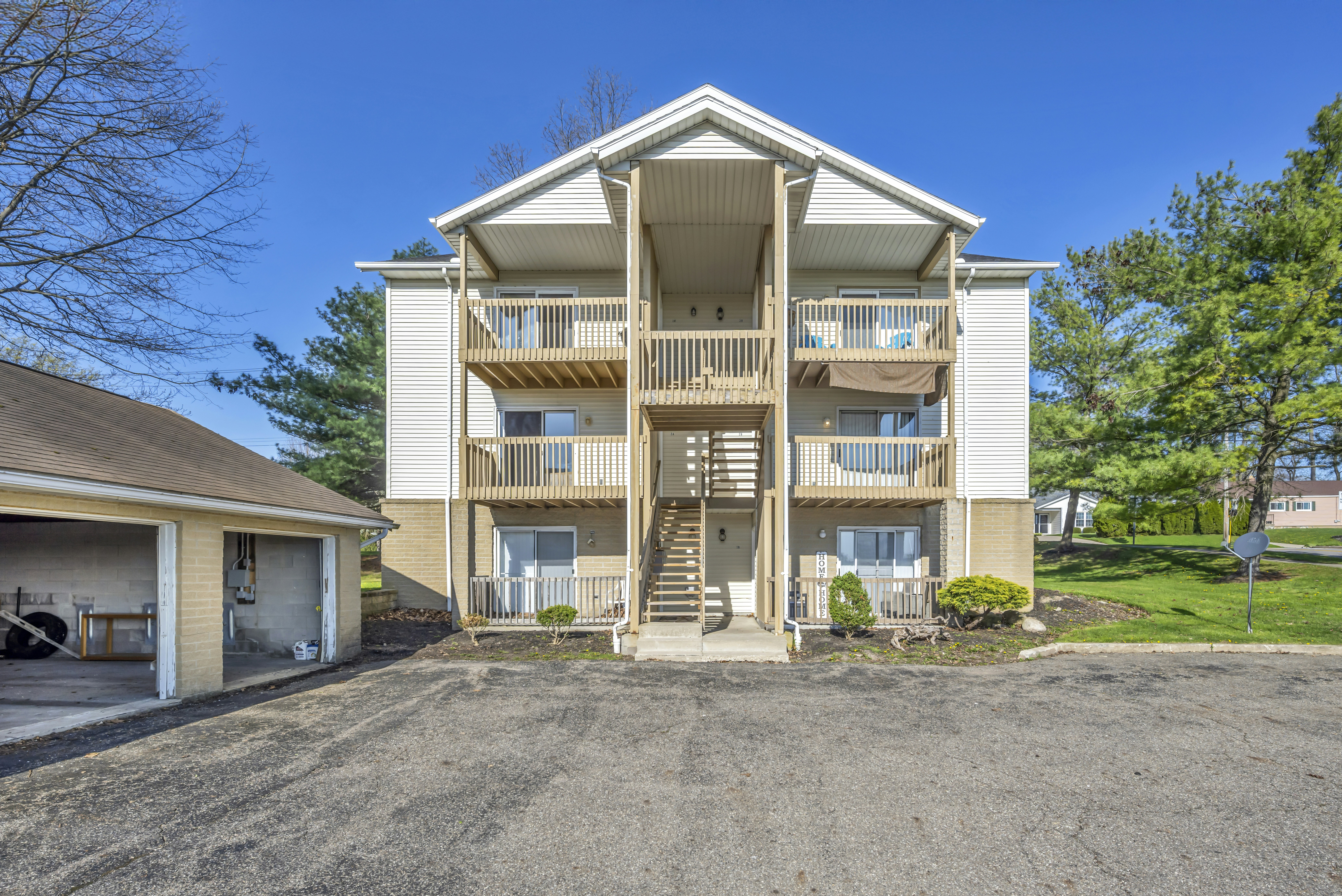 apartment building exterior - A three-story apartment building with wooden balconies and an exterior staircase under blue sky