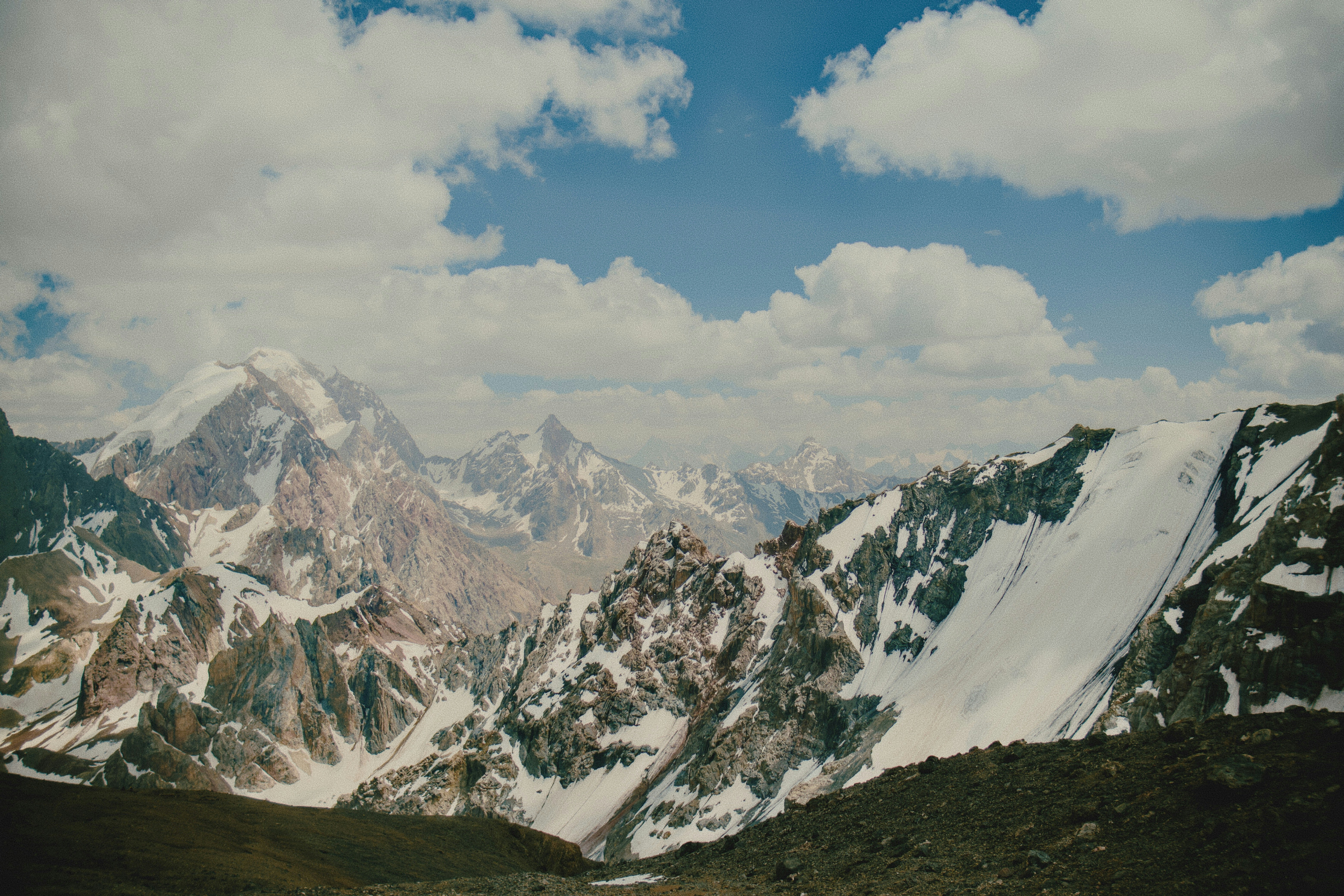 Snow-capped mountain peaks under a blue sky with scattered white clouds