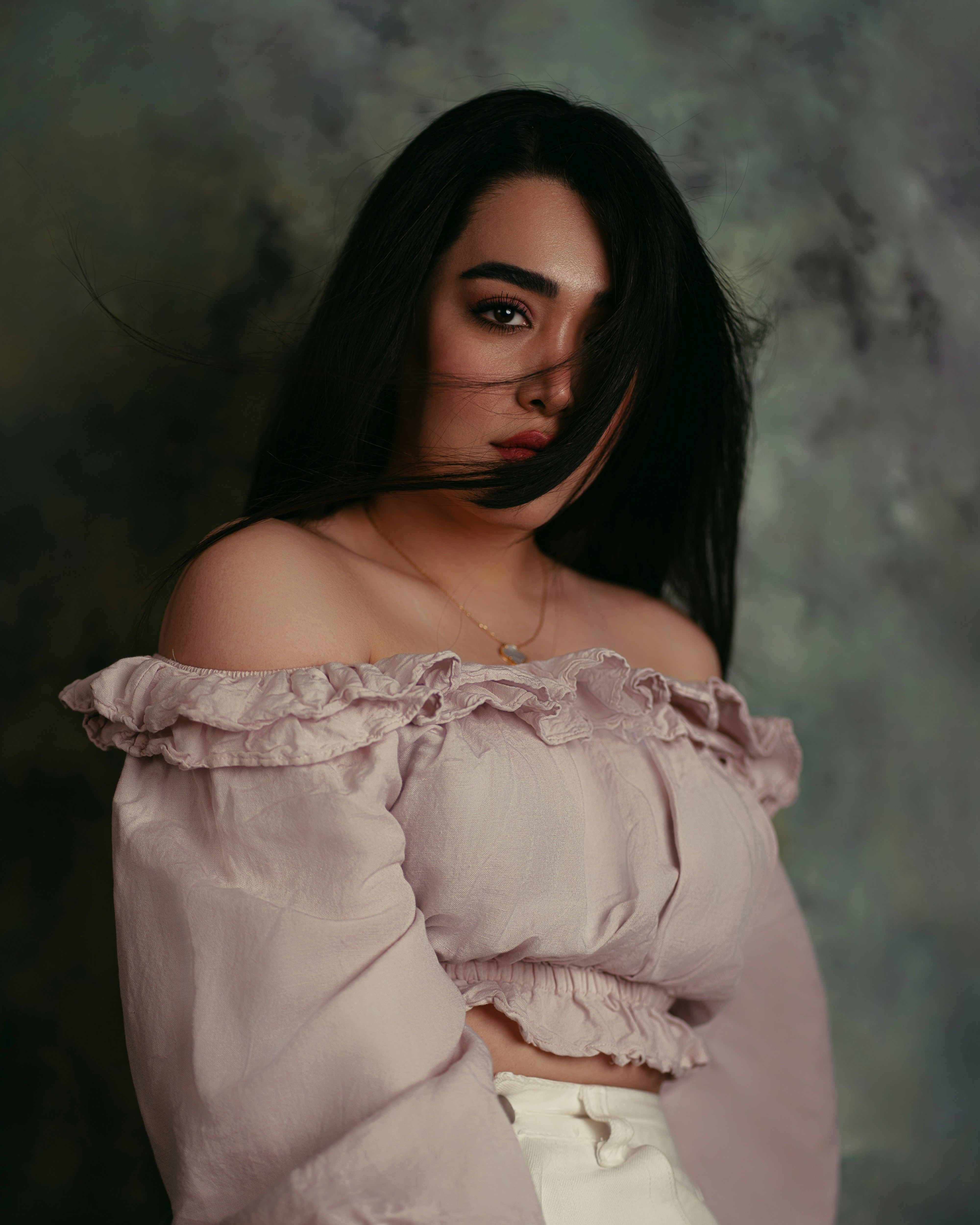 A woman with dark hair wearing a pale pink off-the-shoulder top