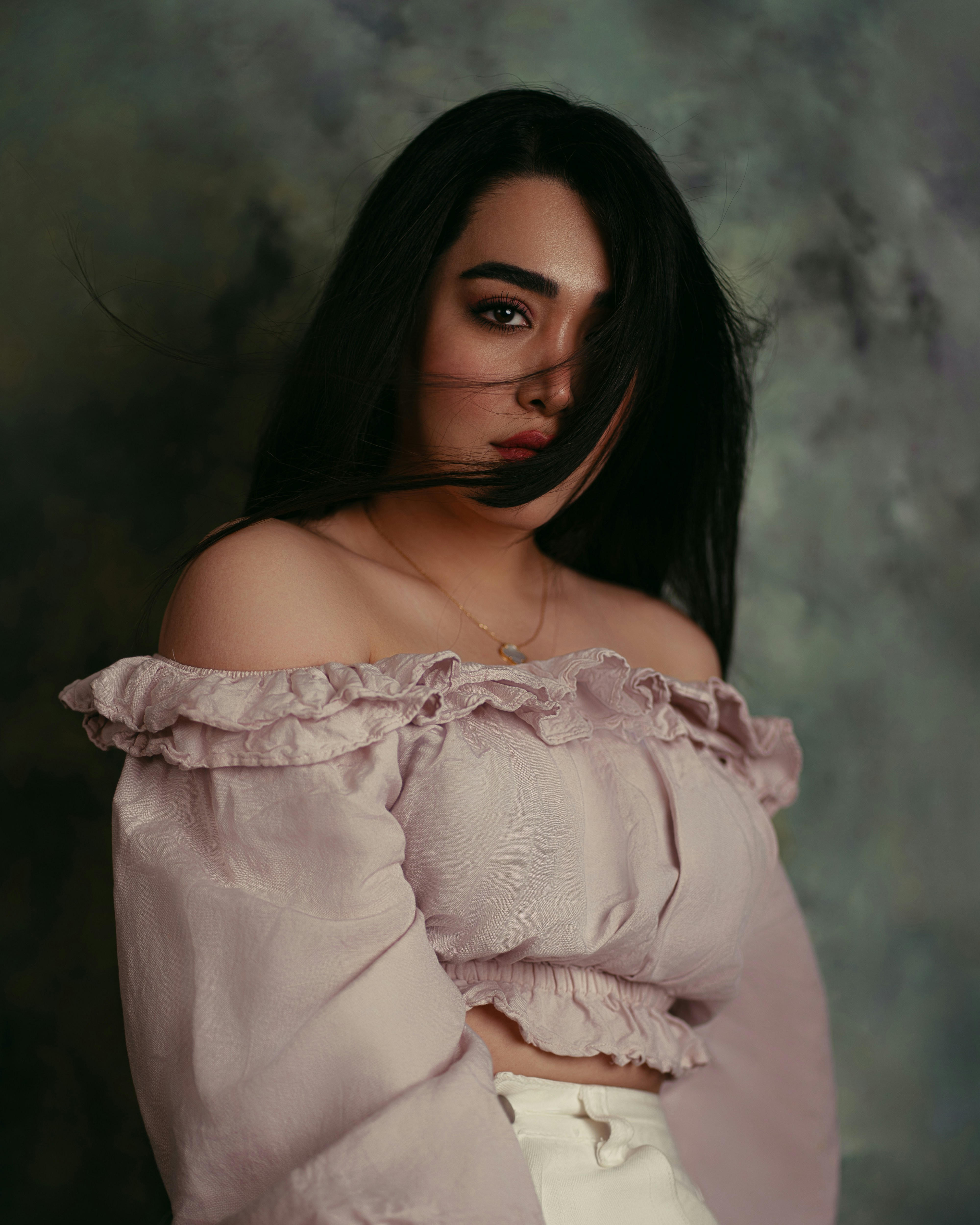 A woman with long dark hair wearing a pale pink off-the-shoulder top