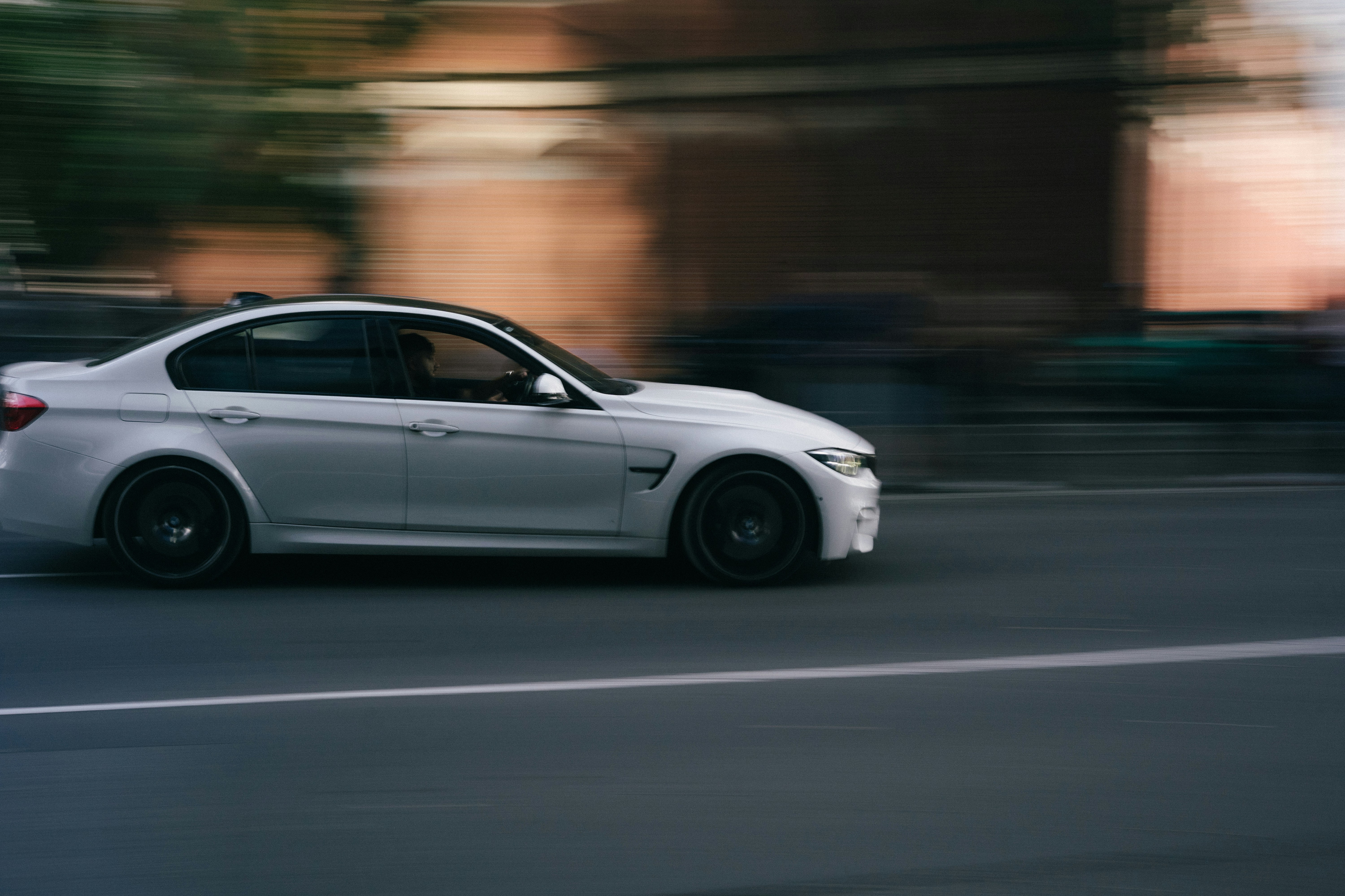 A white sedan driving fast on a city street with motion blur
