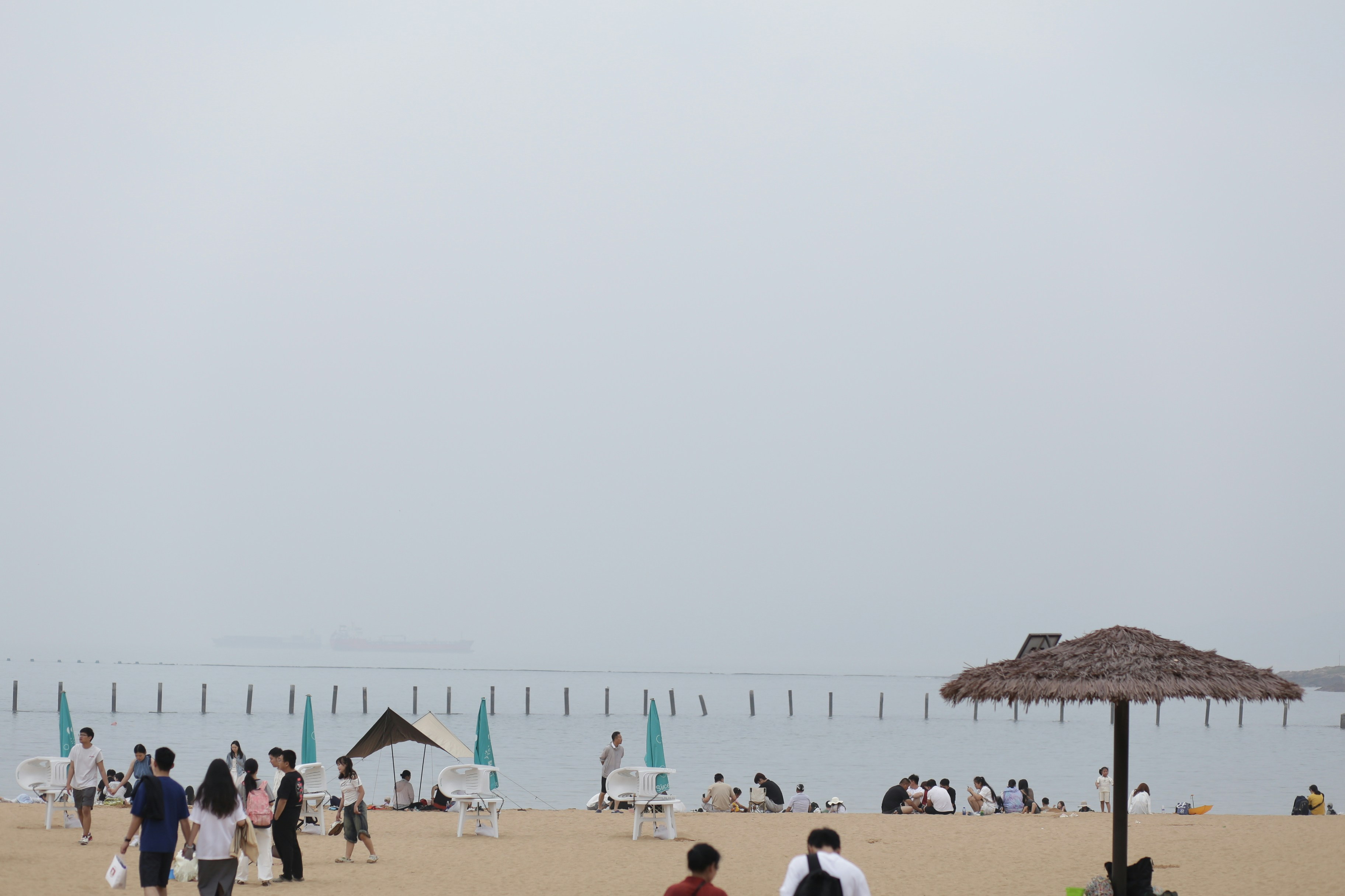 People on a sandy beach with a thatched umbrella under an overcast sky