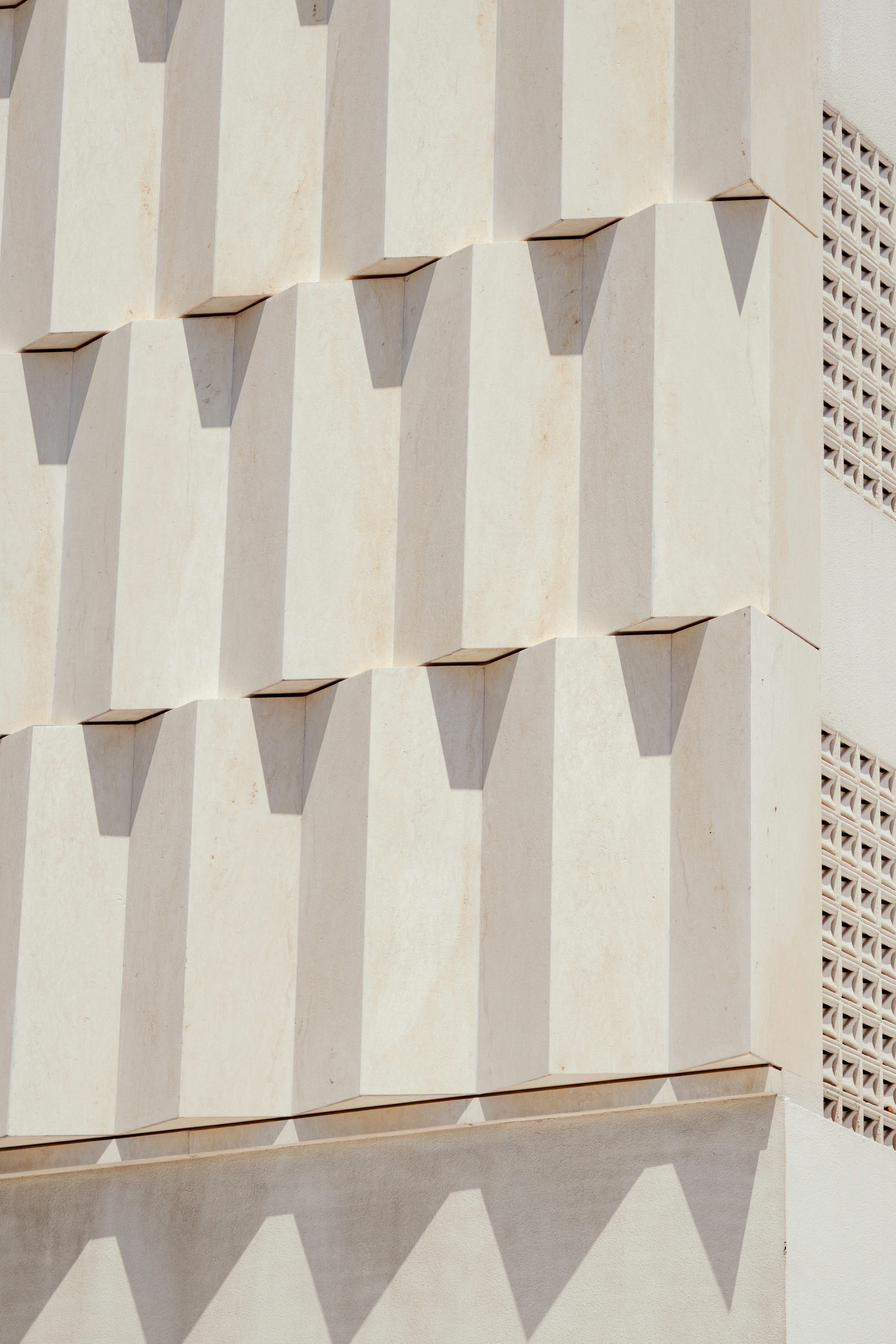 A white building facade with geometric protruding blocks and a decorative lattice screen
