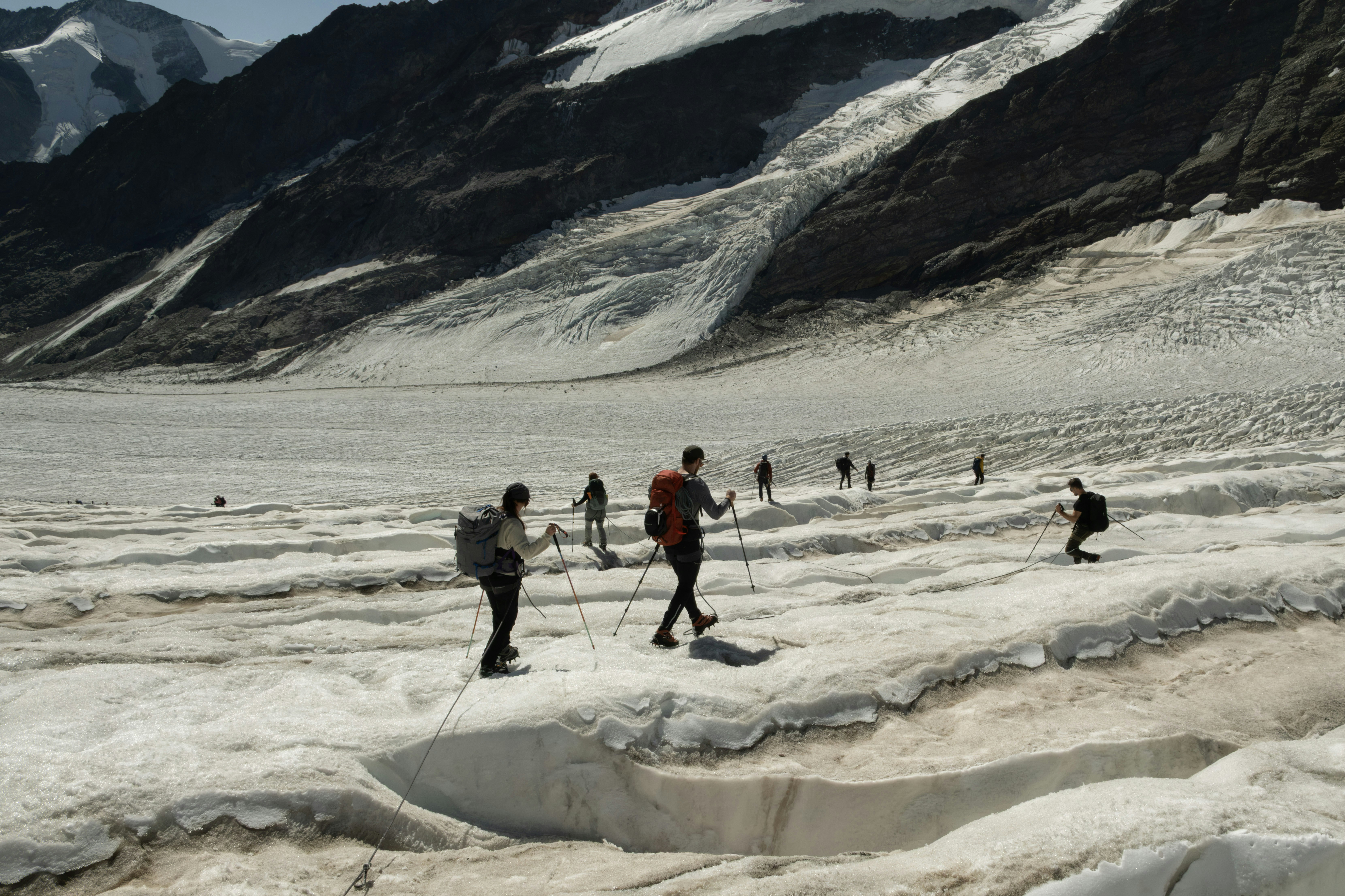 A group of hikers trekking across a vast glacier with rocky mountain peaks