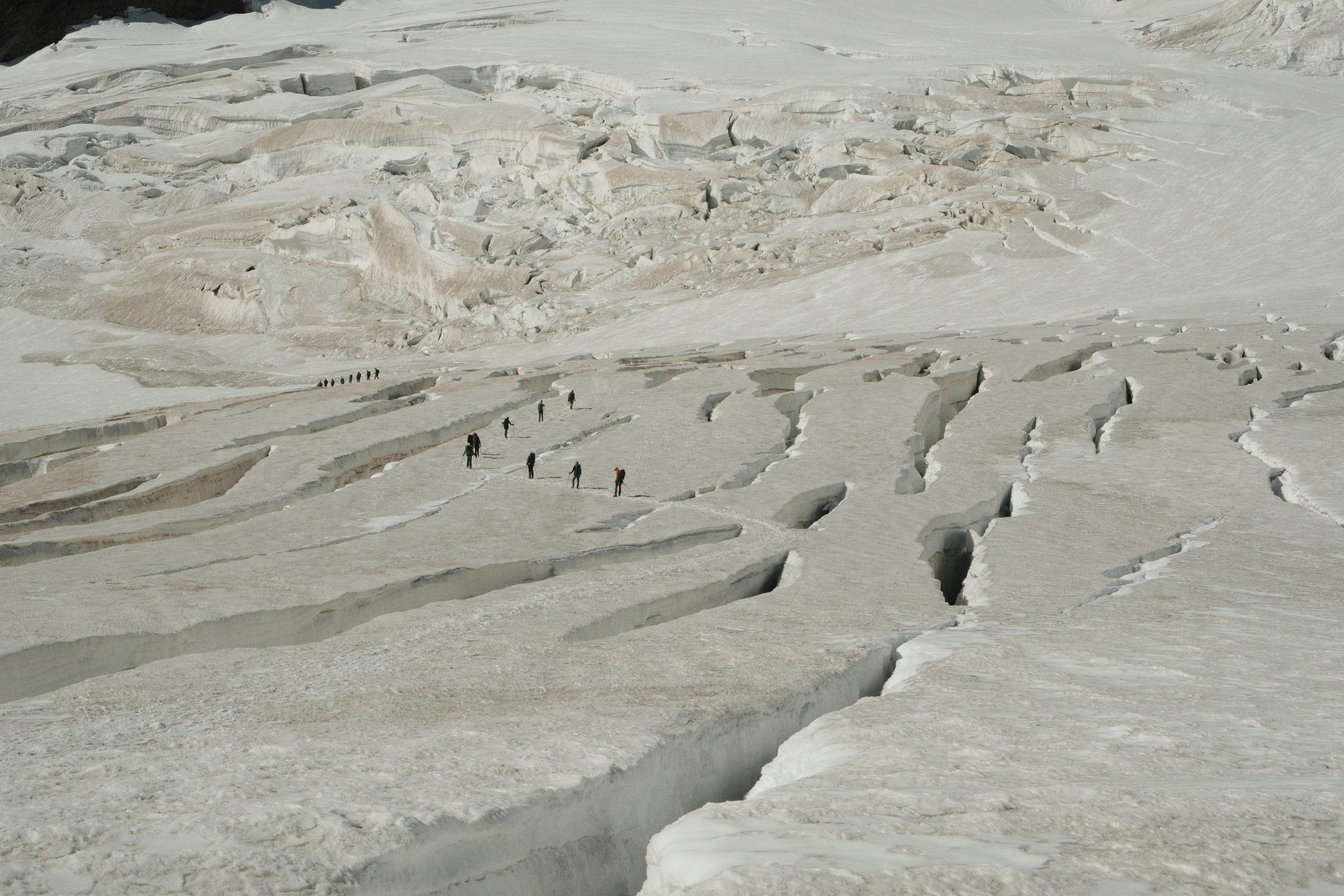 A group of hikers trekking across a vast glacier with deep crevasses