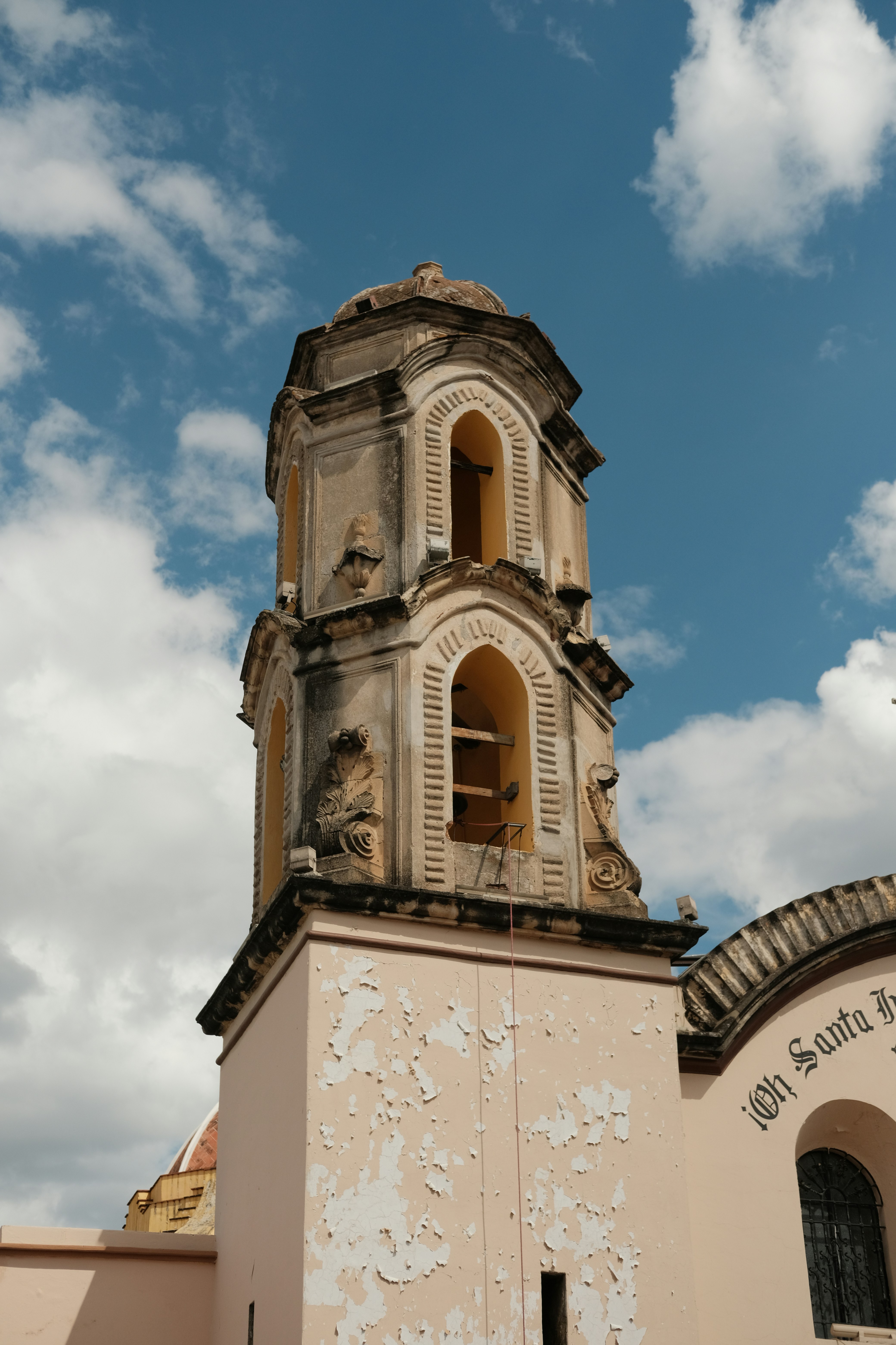 Un campanario desgastado con pintura descascarillada contra un cielo azul con nubes