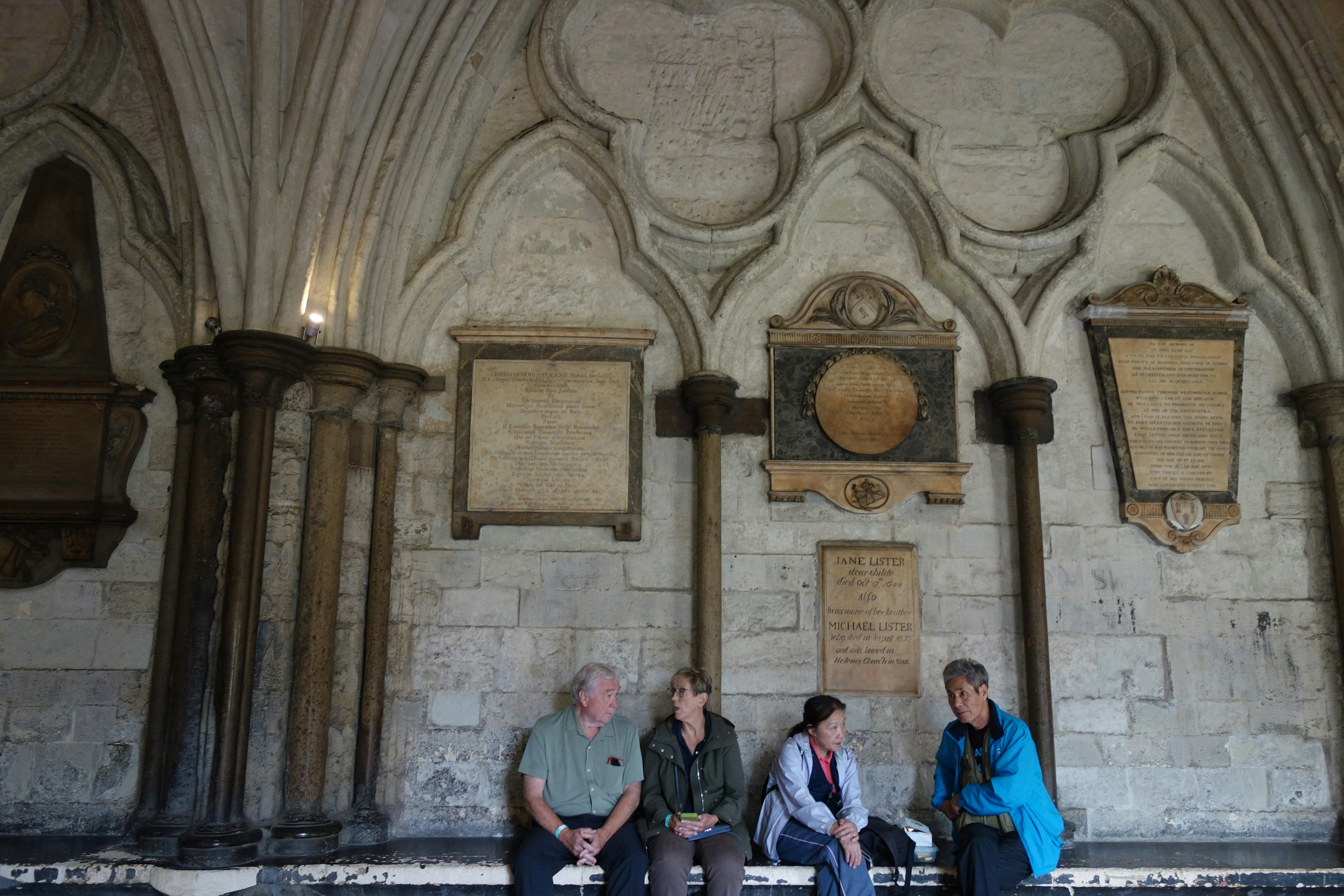 Four people sitting on a stone bench against a wall with memorial plaques - disaster history sites
