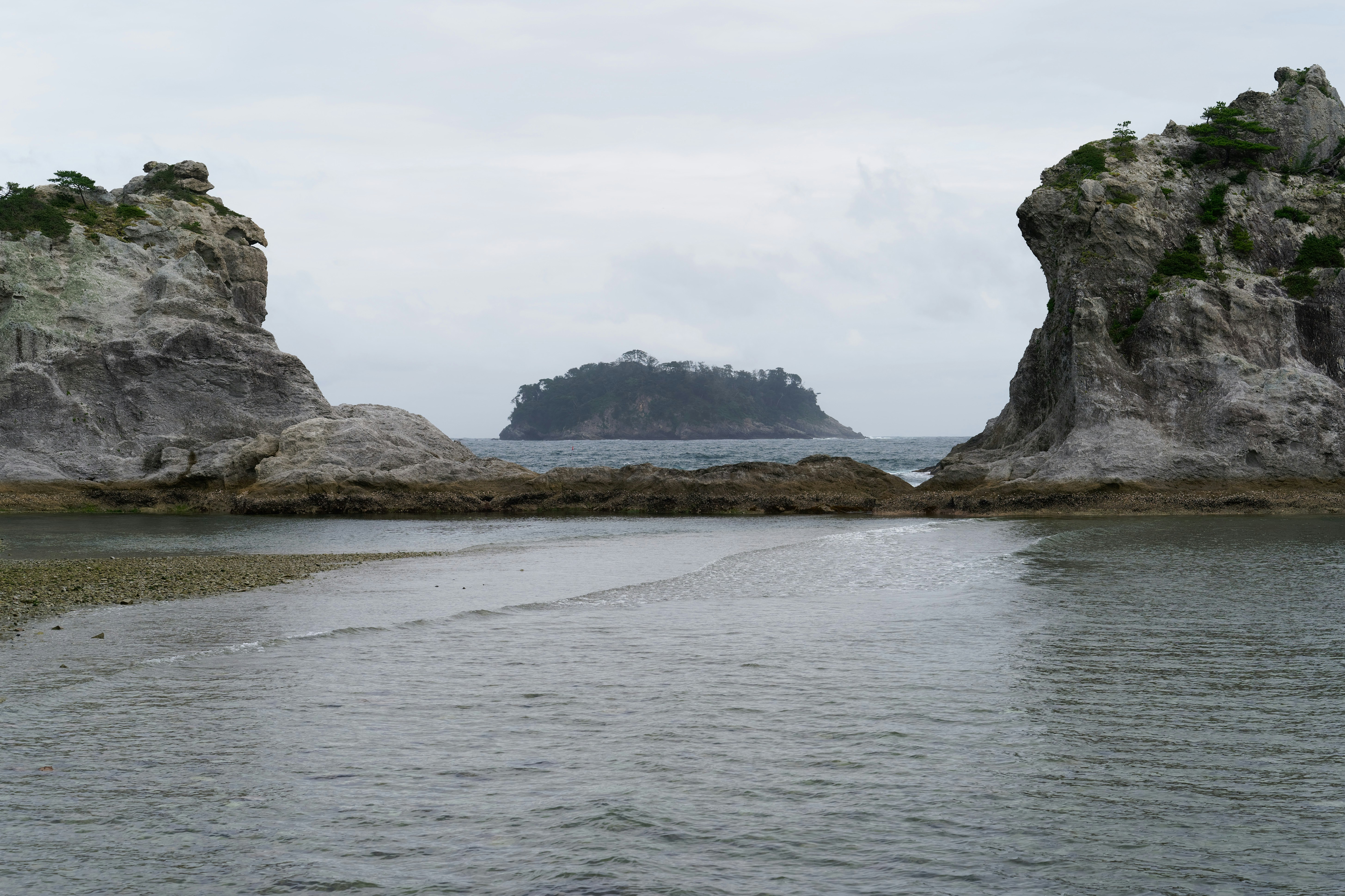 A small island in the distance framed by two large rocky coastal cliffs