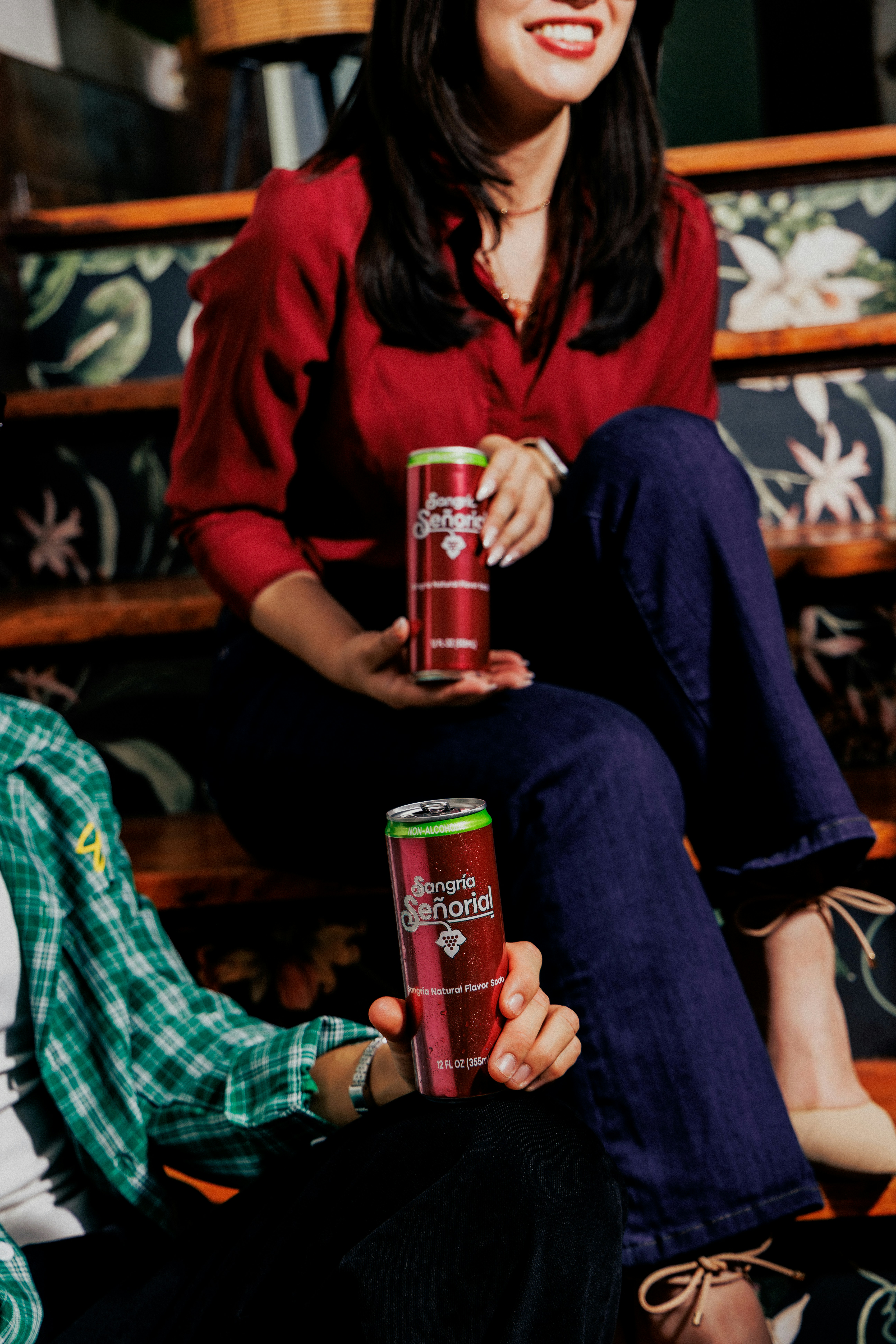 Two people holding cans of Sangria Señorial soda while sitting on wooden stairs