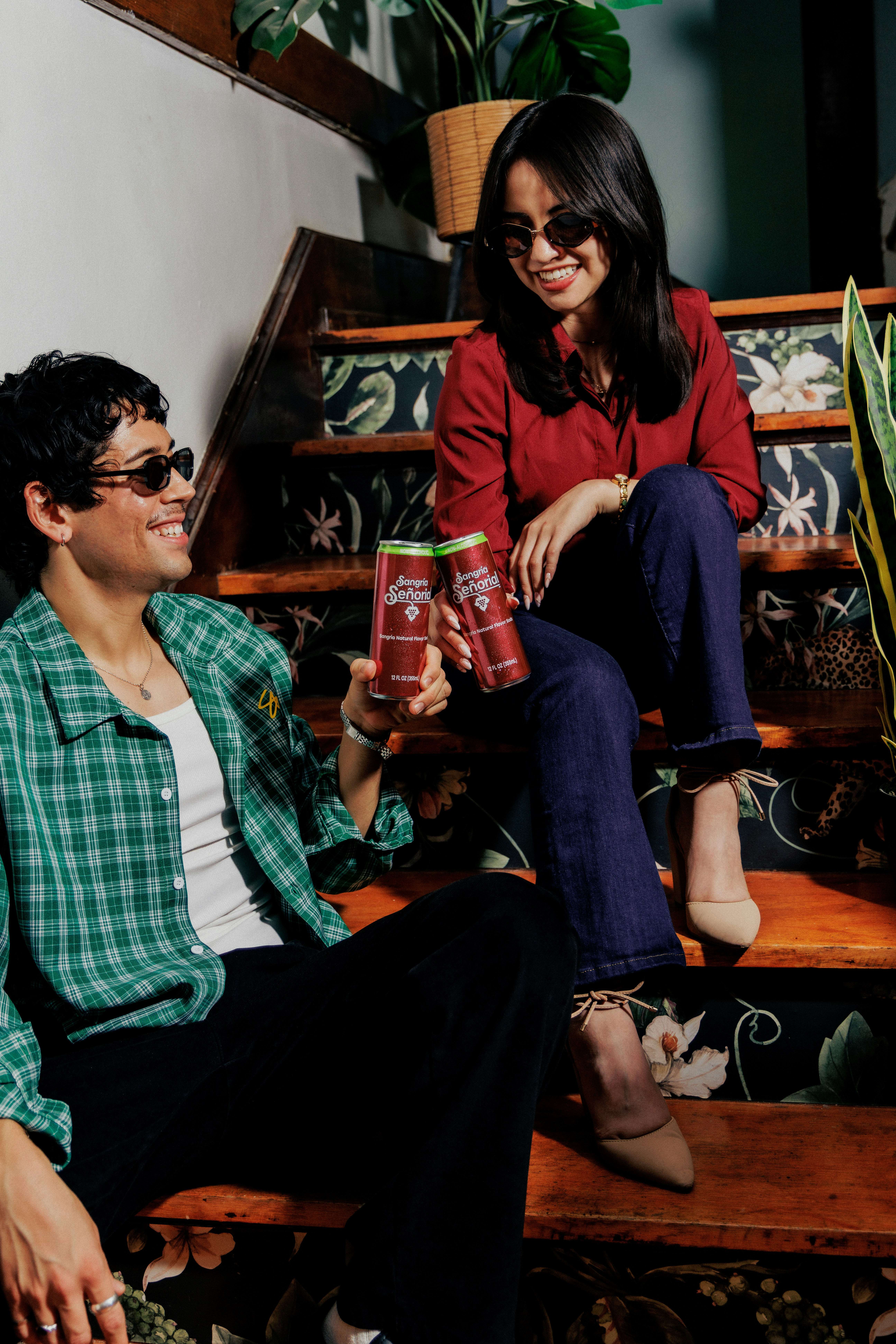 A man and a woman sitting on wooden stairs holding cans of Sangria Señorial