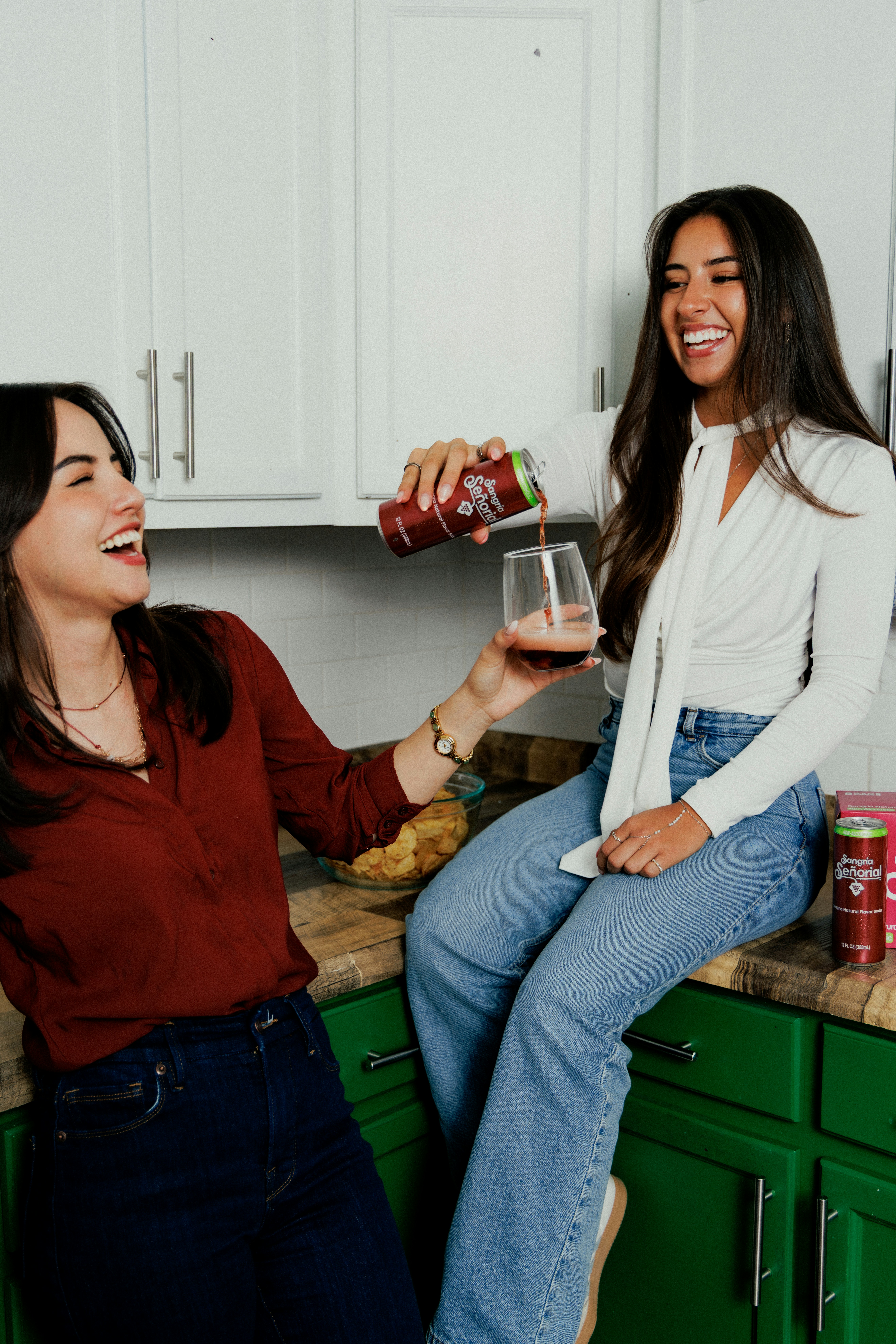 A woman pouring a drink into a glass for a friend in a kitchen