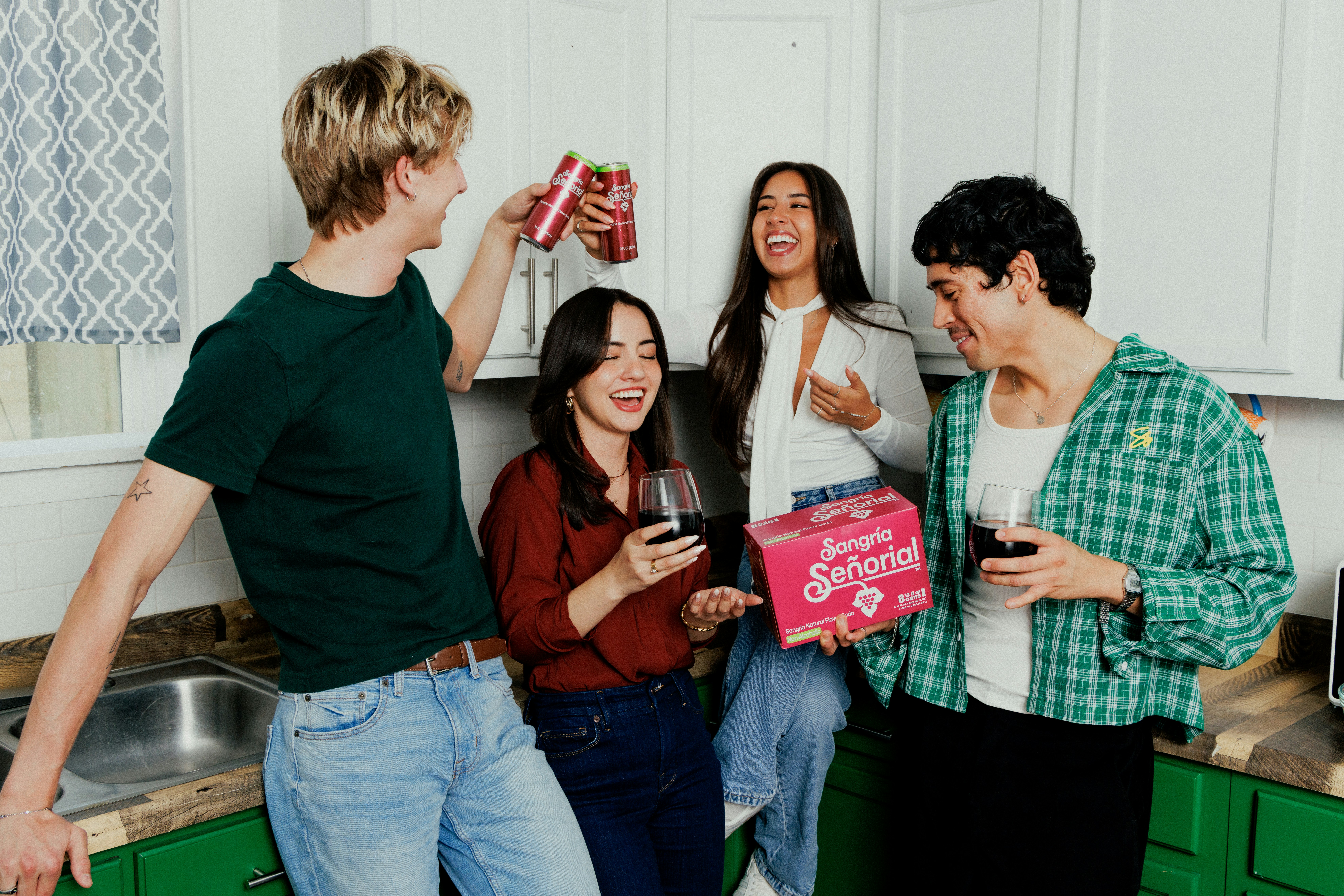 A group of four people laughing and holding drinks in a kitchen