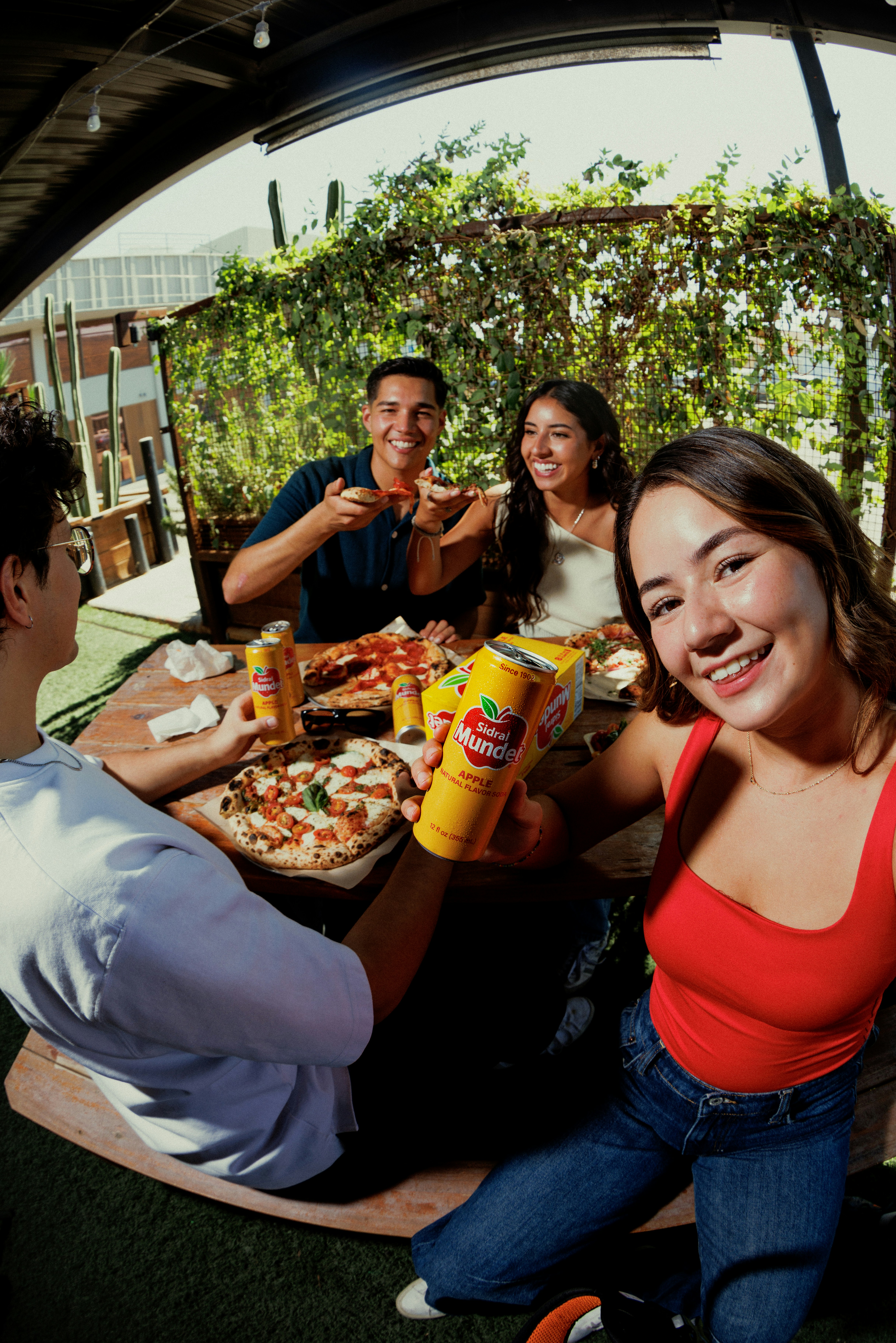 A group of four people eating pizza and drinking soda at an outdoor table