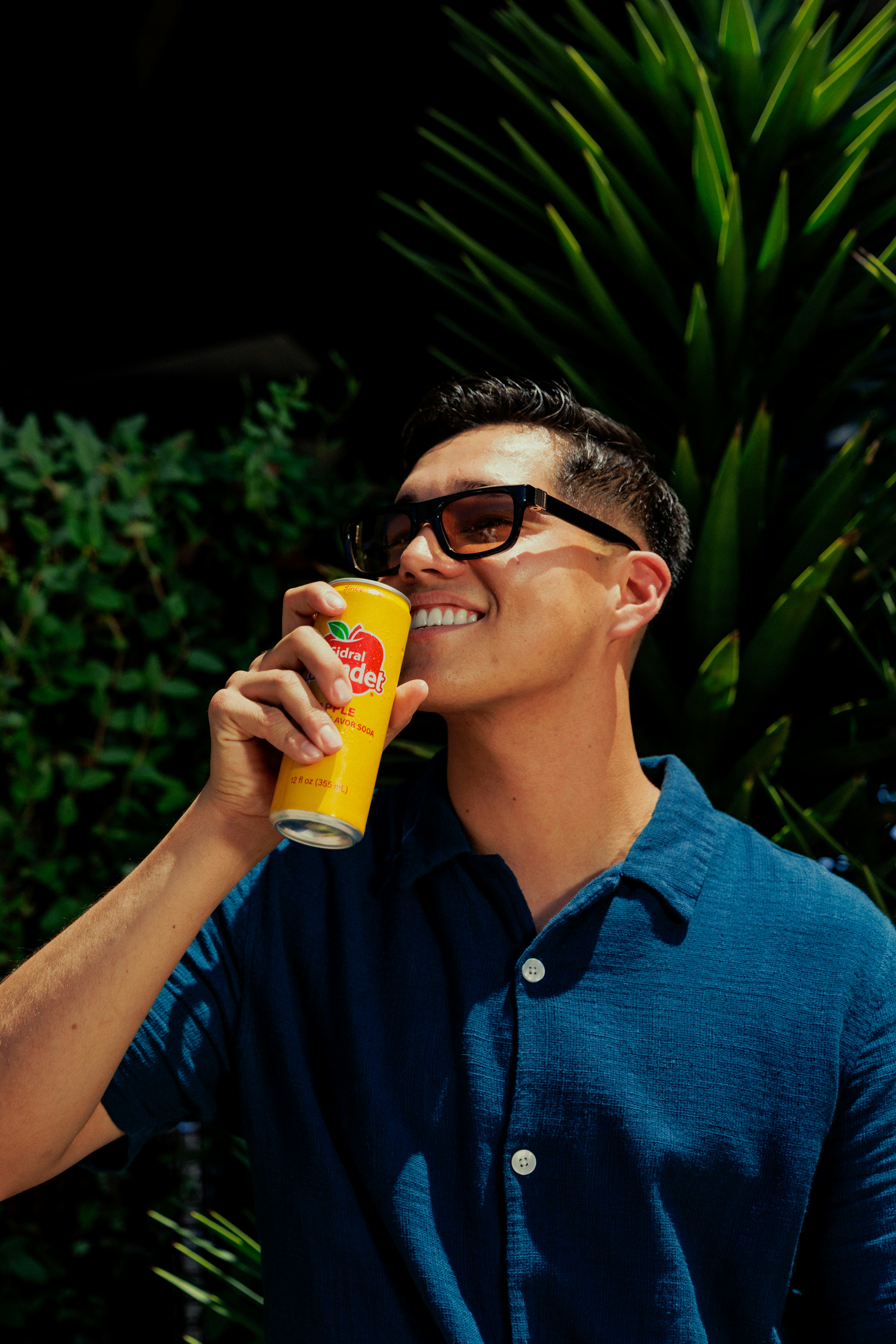 A man in a blue shirt drinking from a yellow soda can outdoors