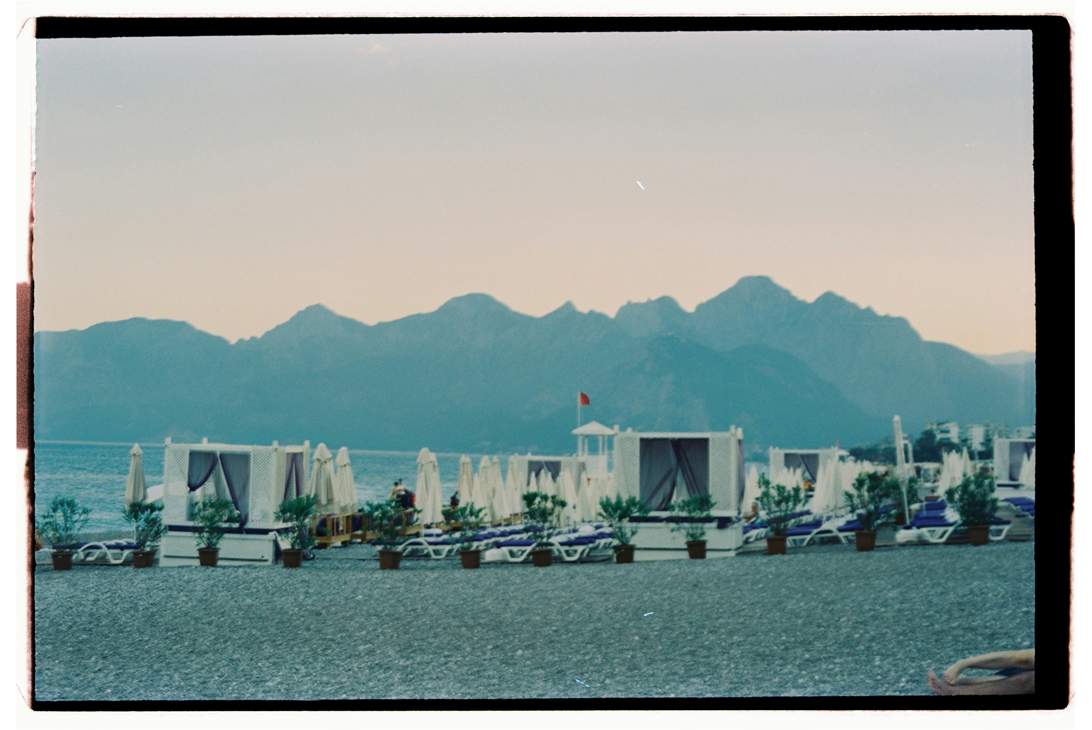 Cabanas and lounge chairs on a pebble beach before distant blue mountains