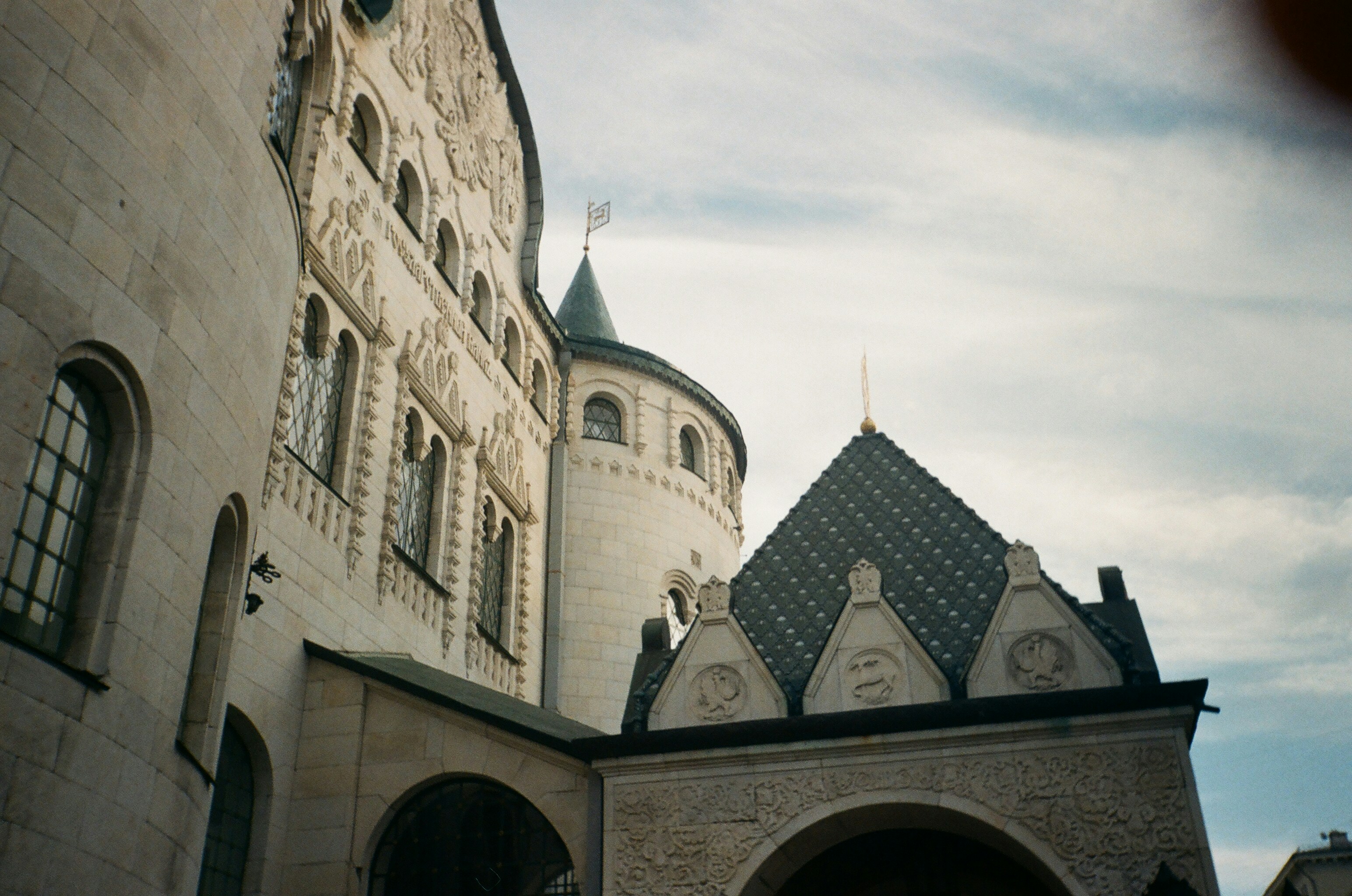 Ornate stone architecture with arched windows and a tiled roof under a cloudy sky