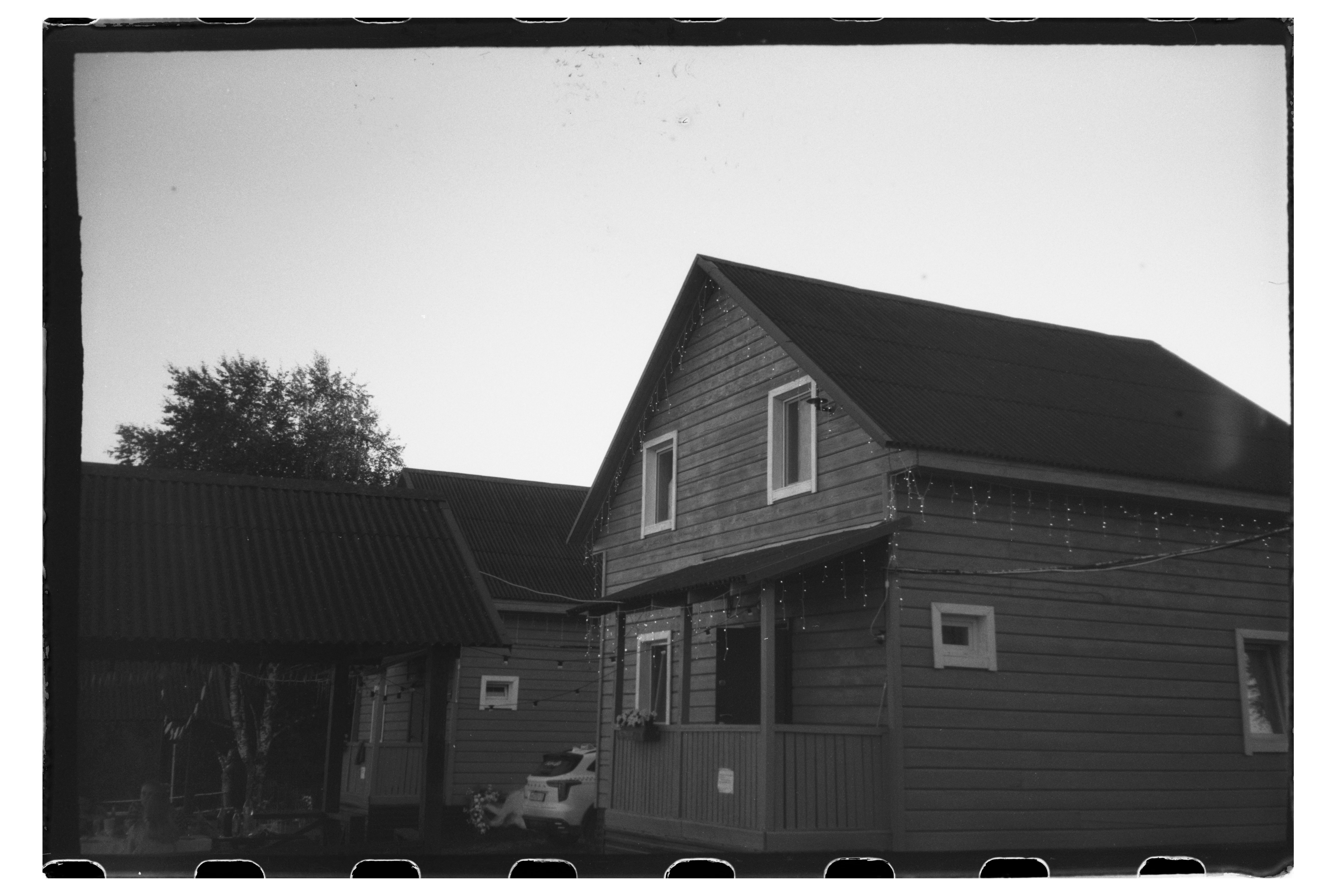Two wooden houses with gabled roofs and string lights in a rural setting