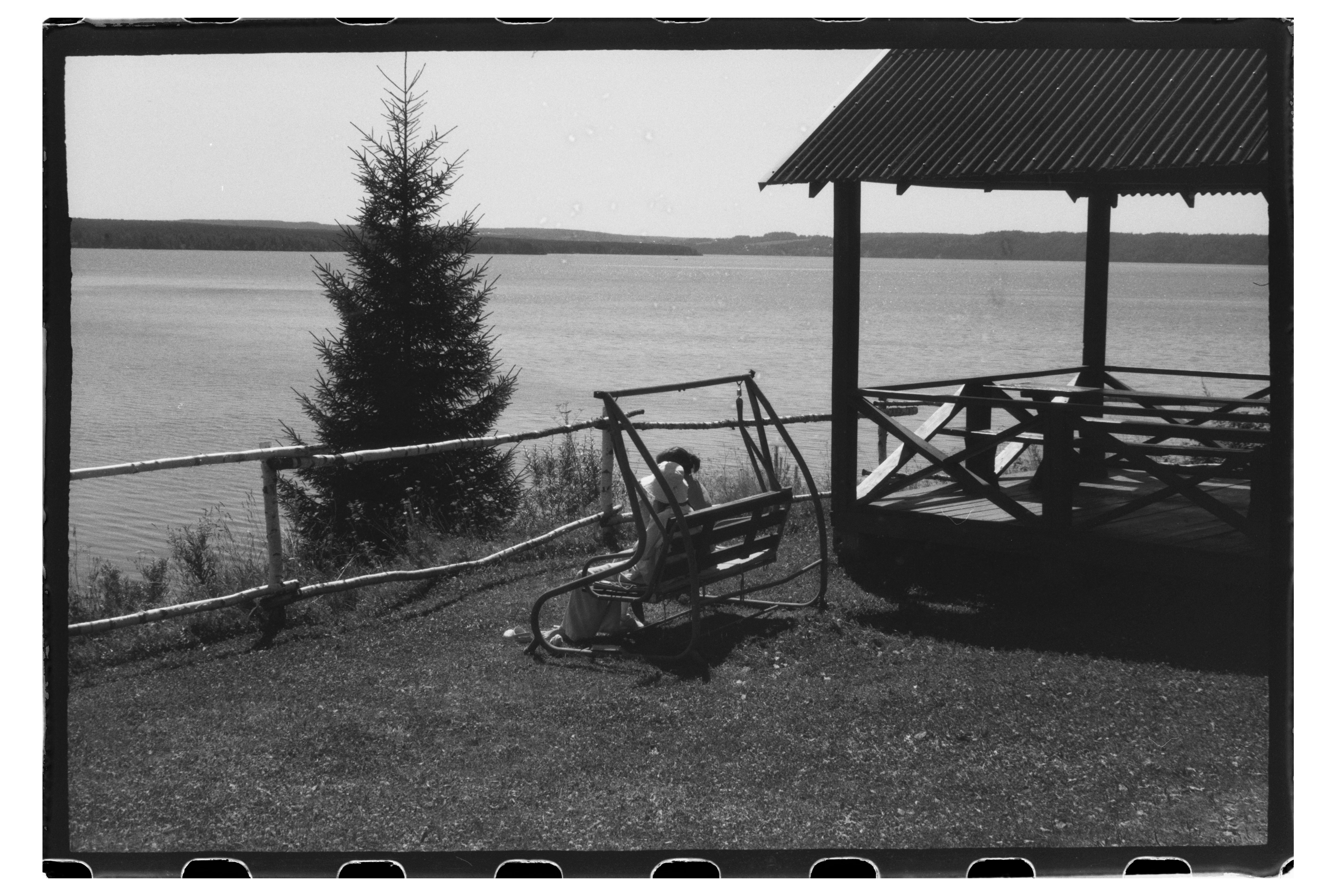 A person on a swing beside a gazebo overlooking a large lake