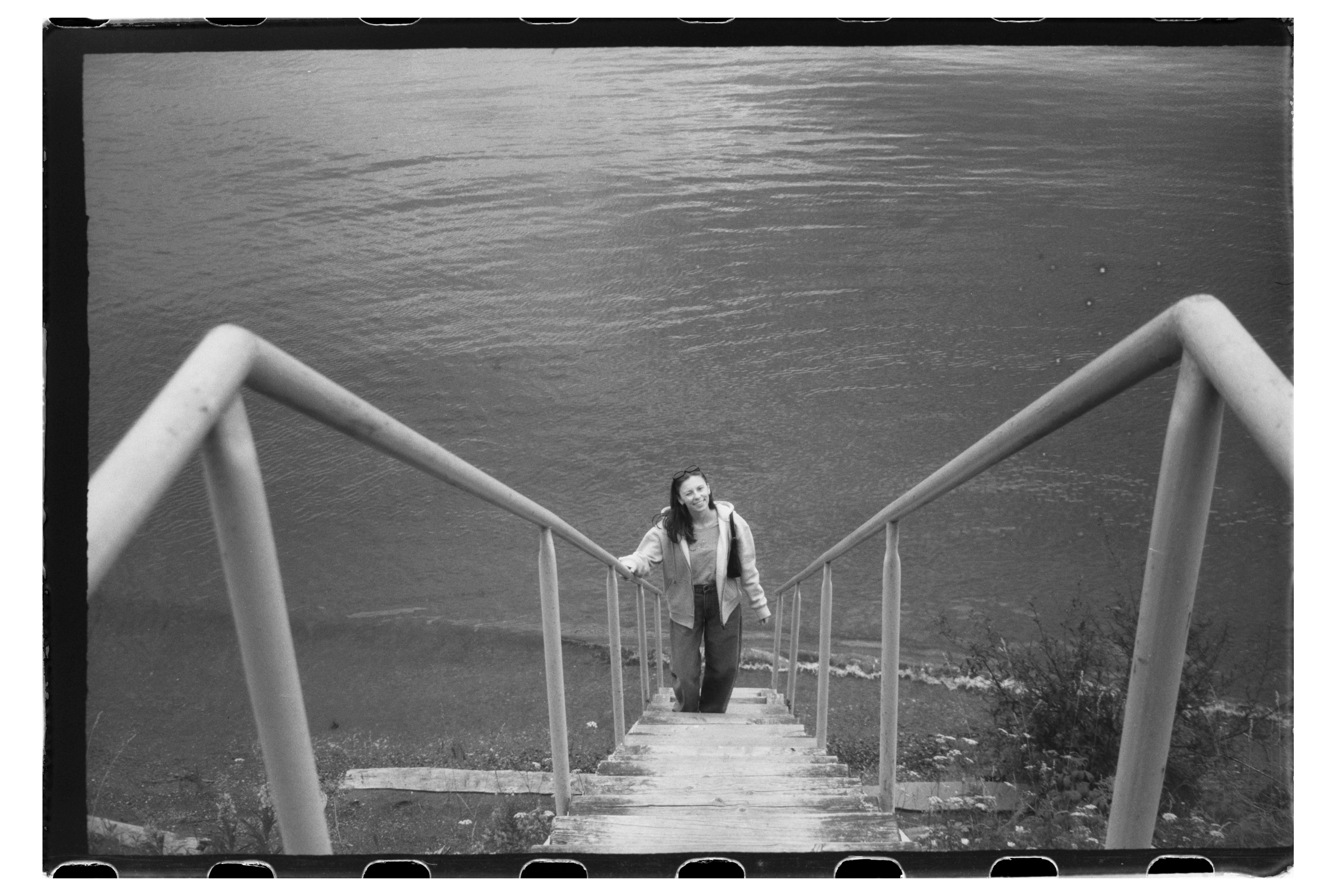 A woman in a hoodie and jeans walking up wooden stairs by water