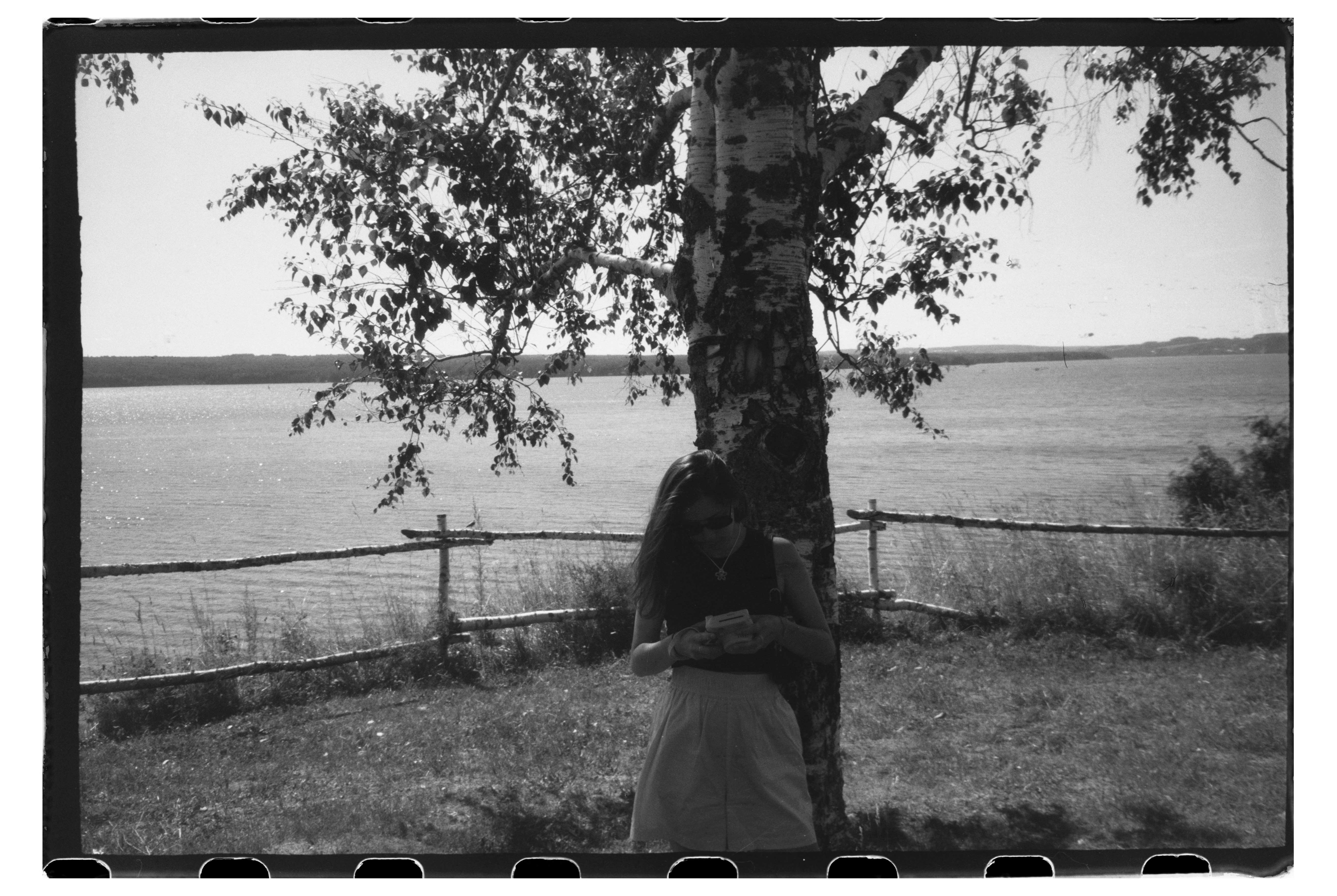 A woman in a dark top and skirt standing by a birch tree