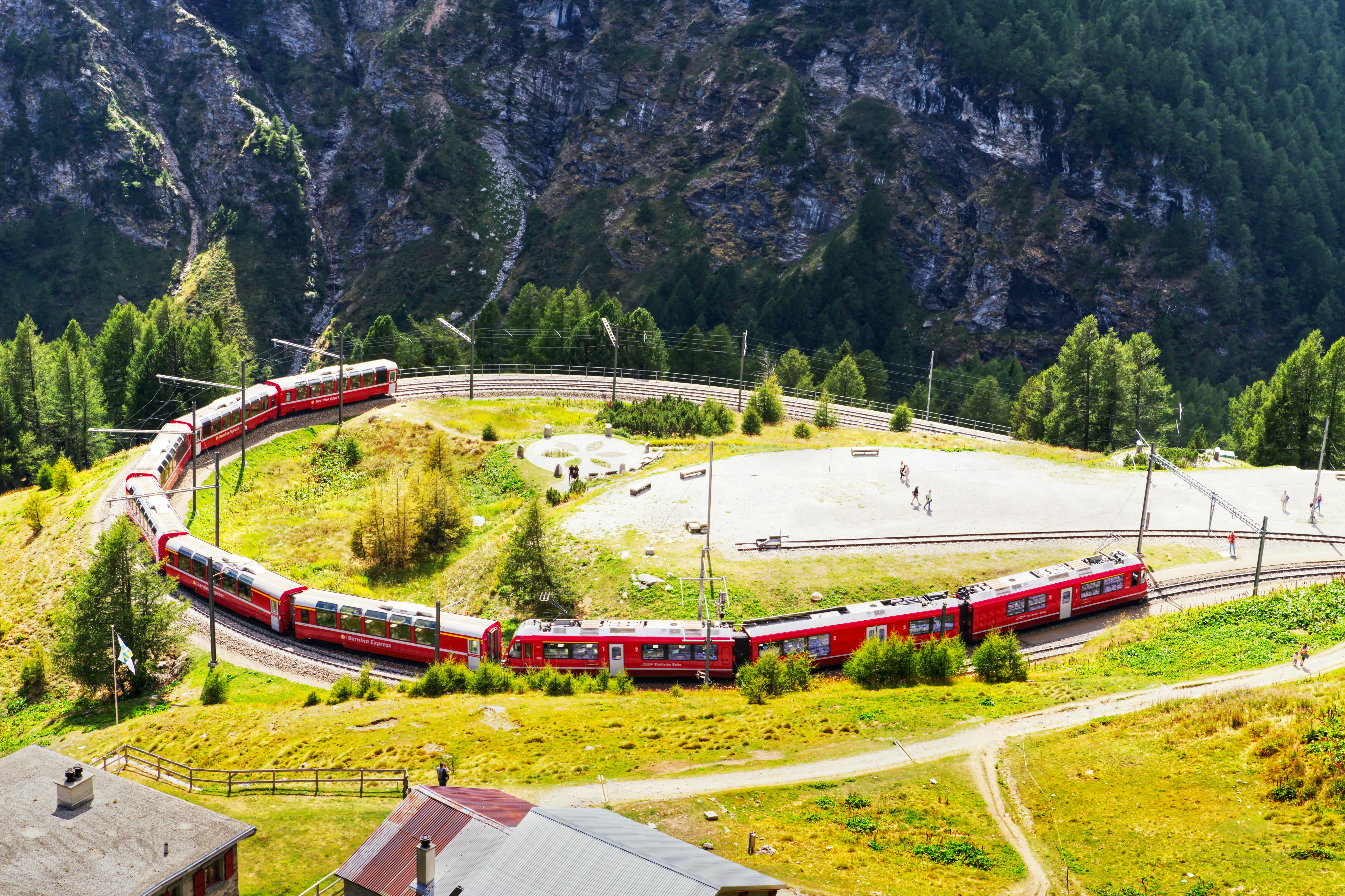 A red Bernina Express train curving along tracks in the Swiss Alps