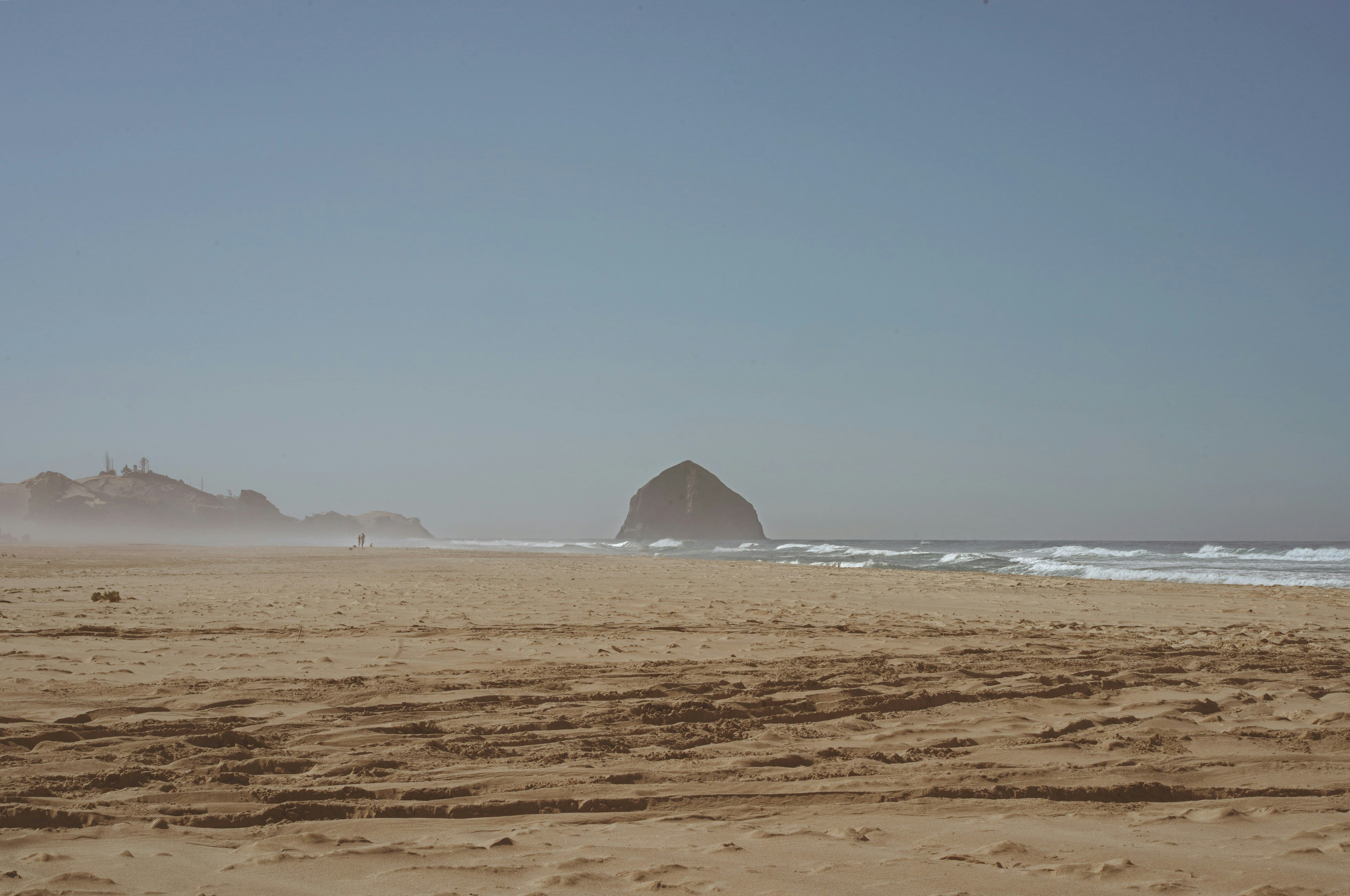 A large sea stack on a sandy beach with gentle waves and mist