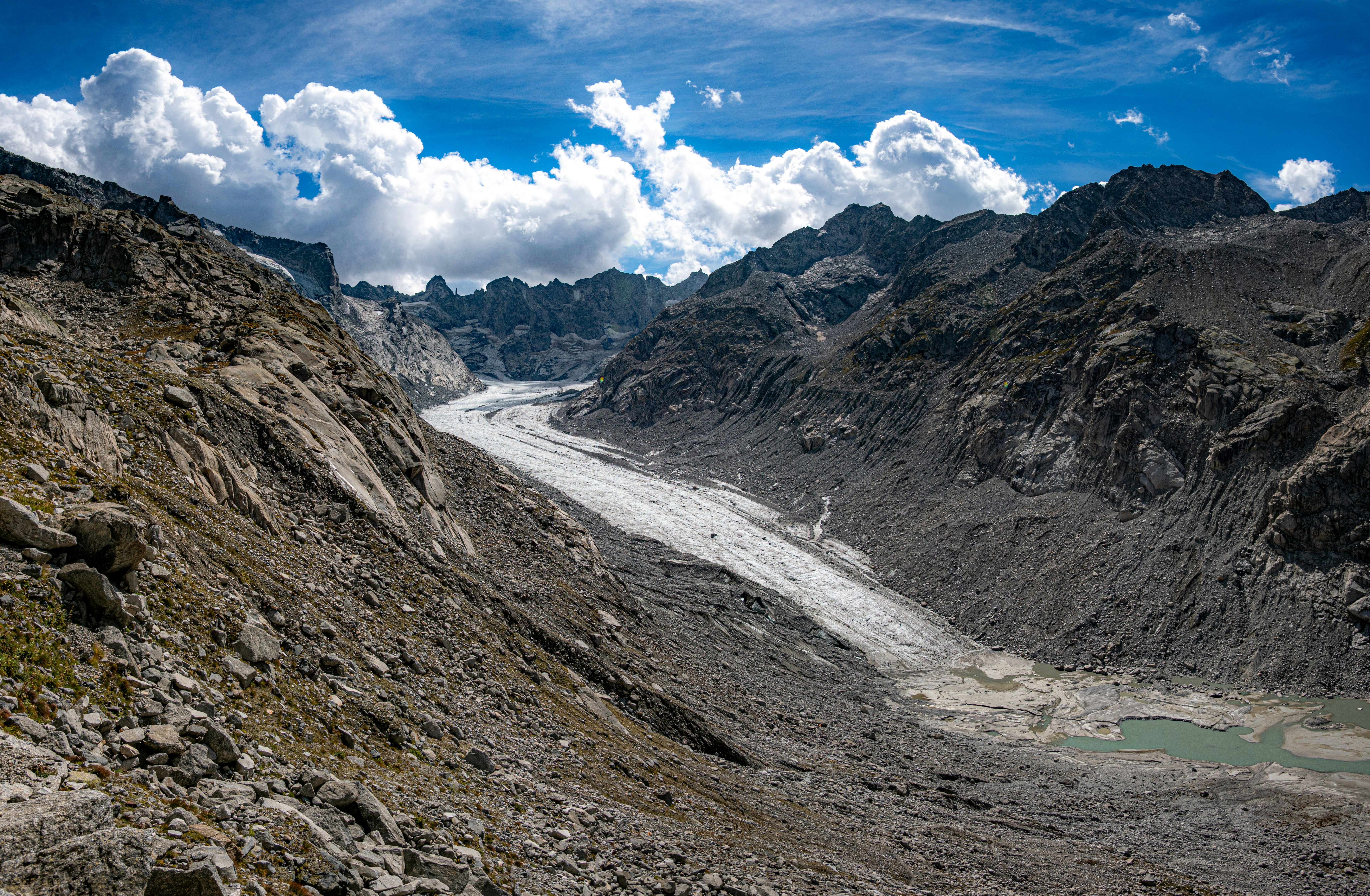 A glacier flowing through a rocky mountain valley under a bright blue sky