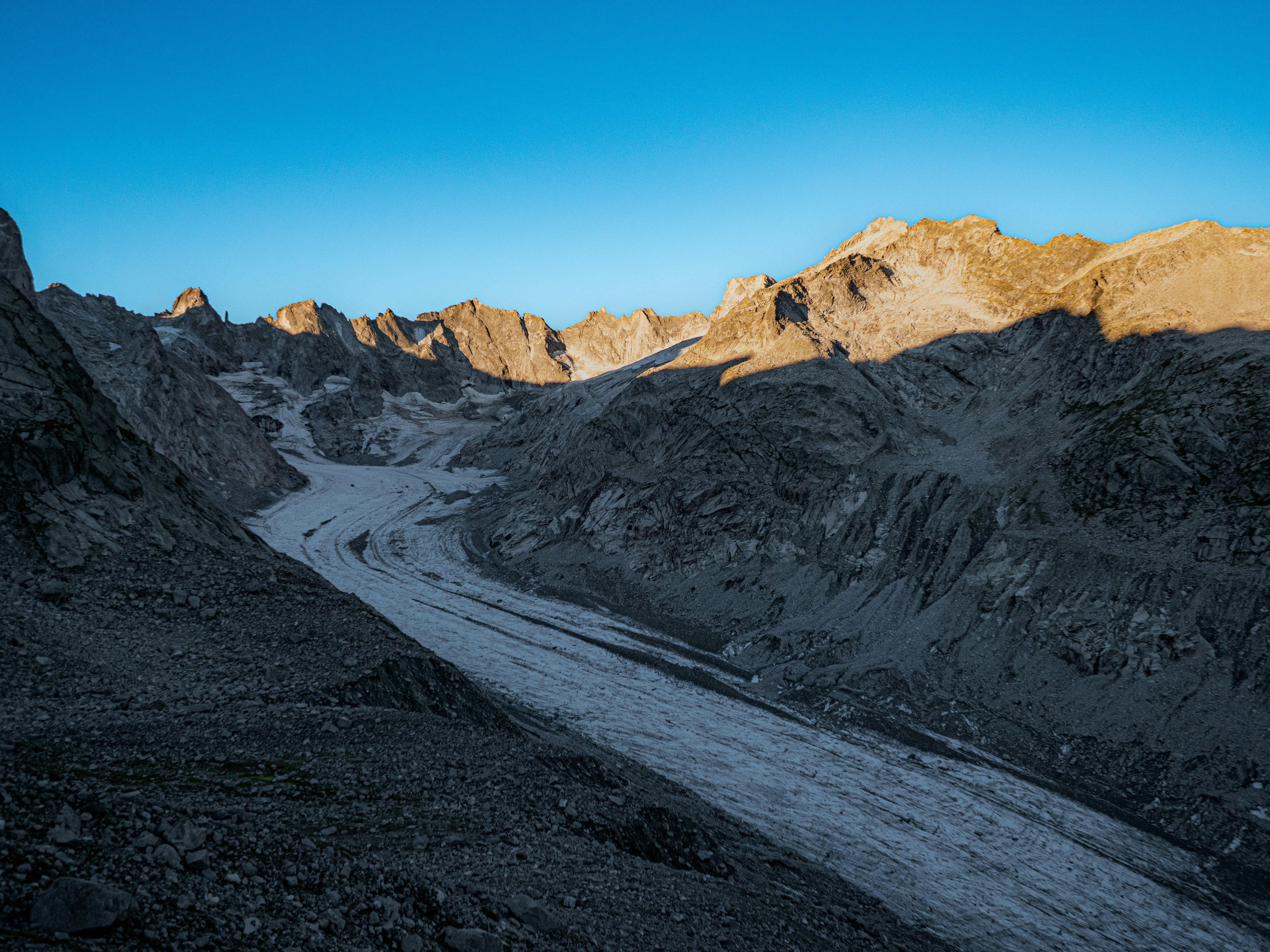 A glacier flowing through a rocky mountain valley under a clear blue sky