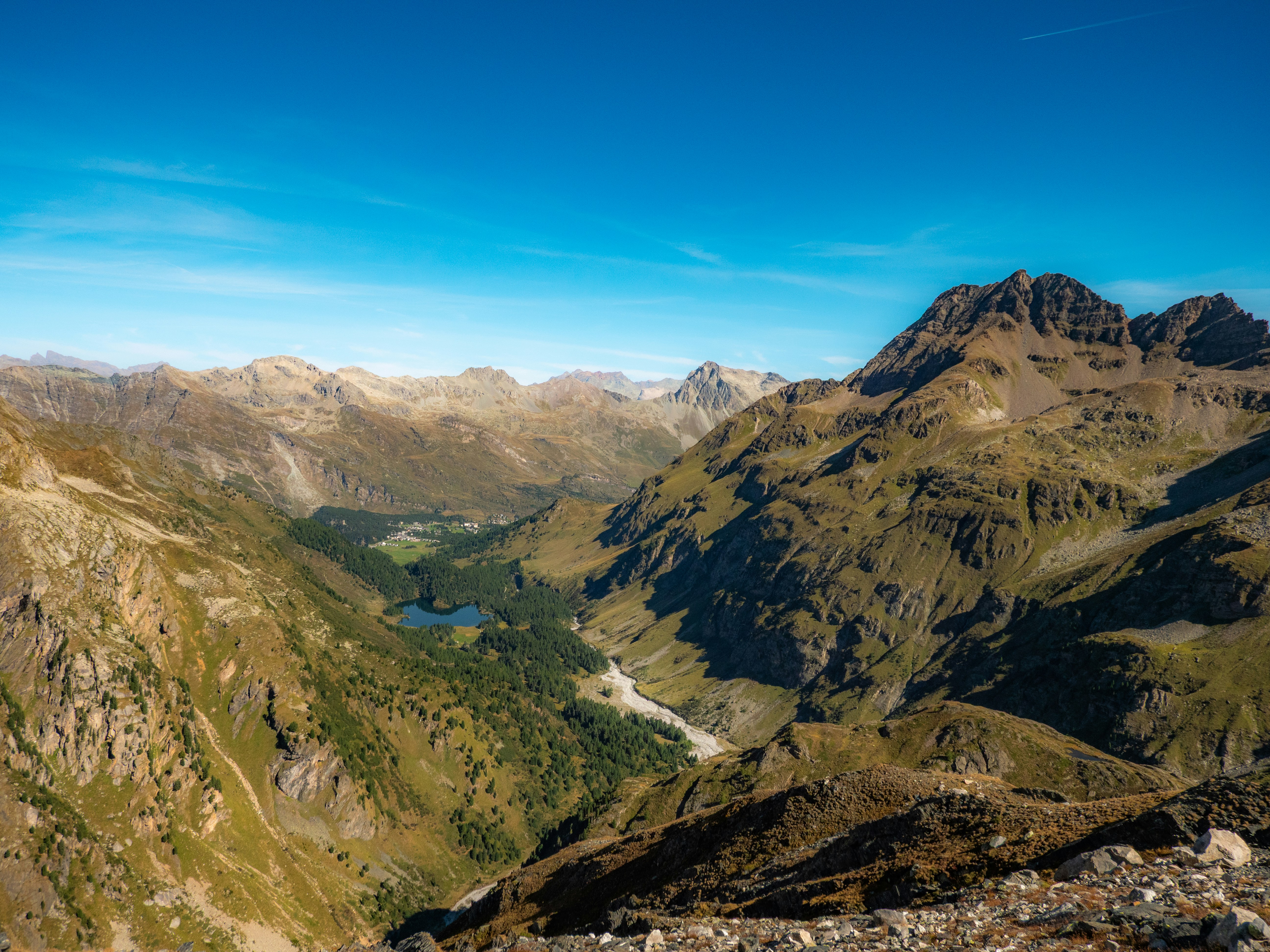 A deep mountain valley with a small lake and forest under a clear blue sky