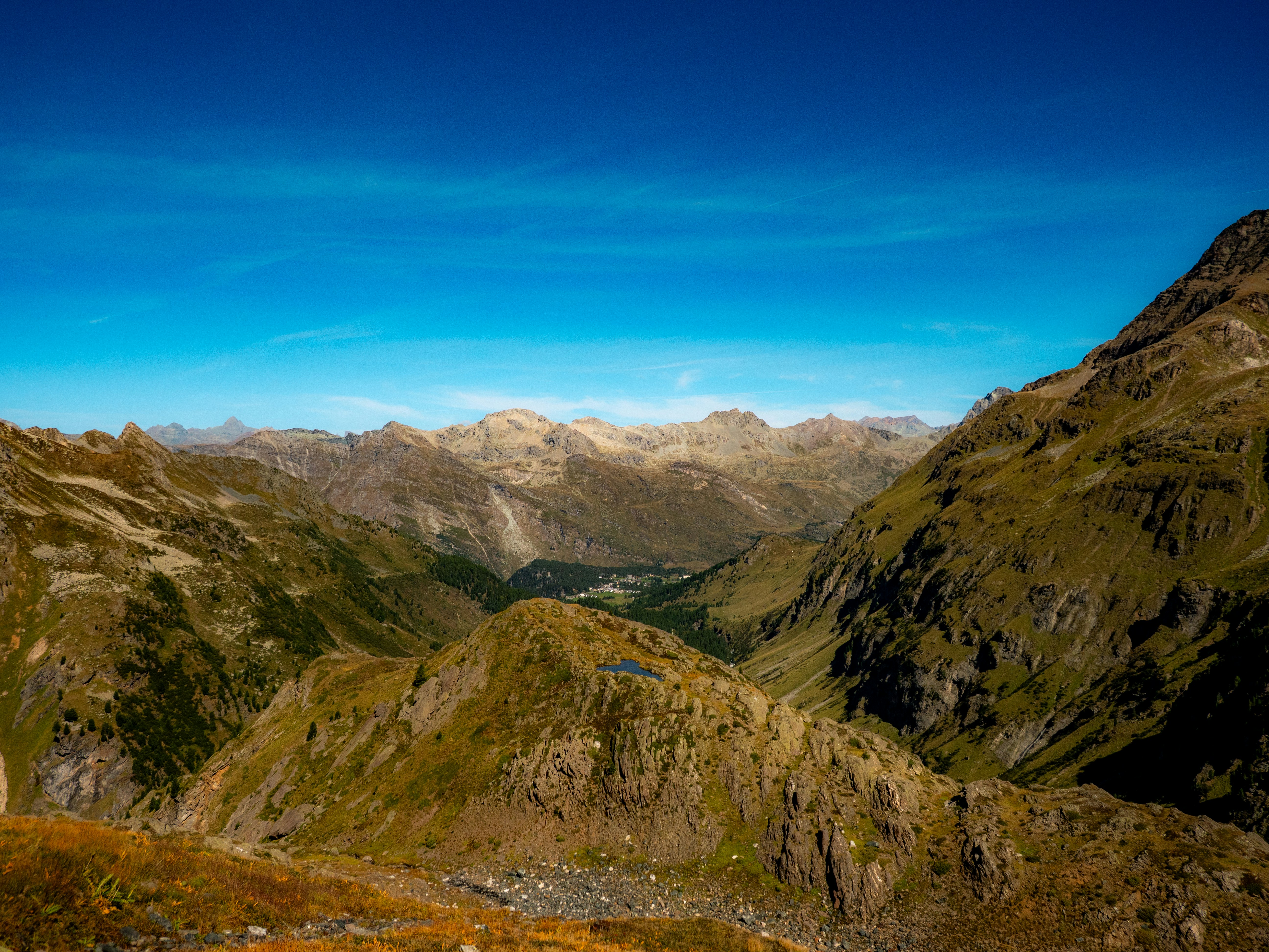 A vast mountain valley with rocky slopes and a small lake under blue sky