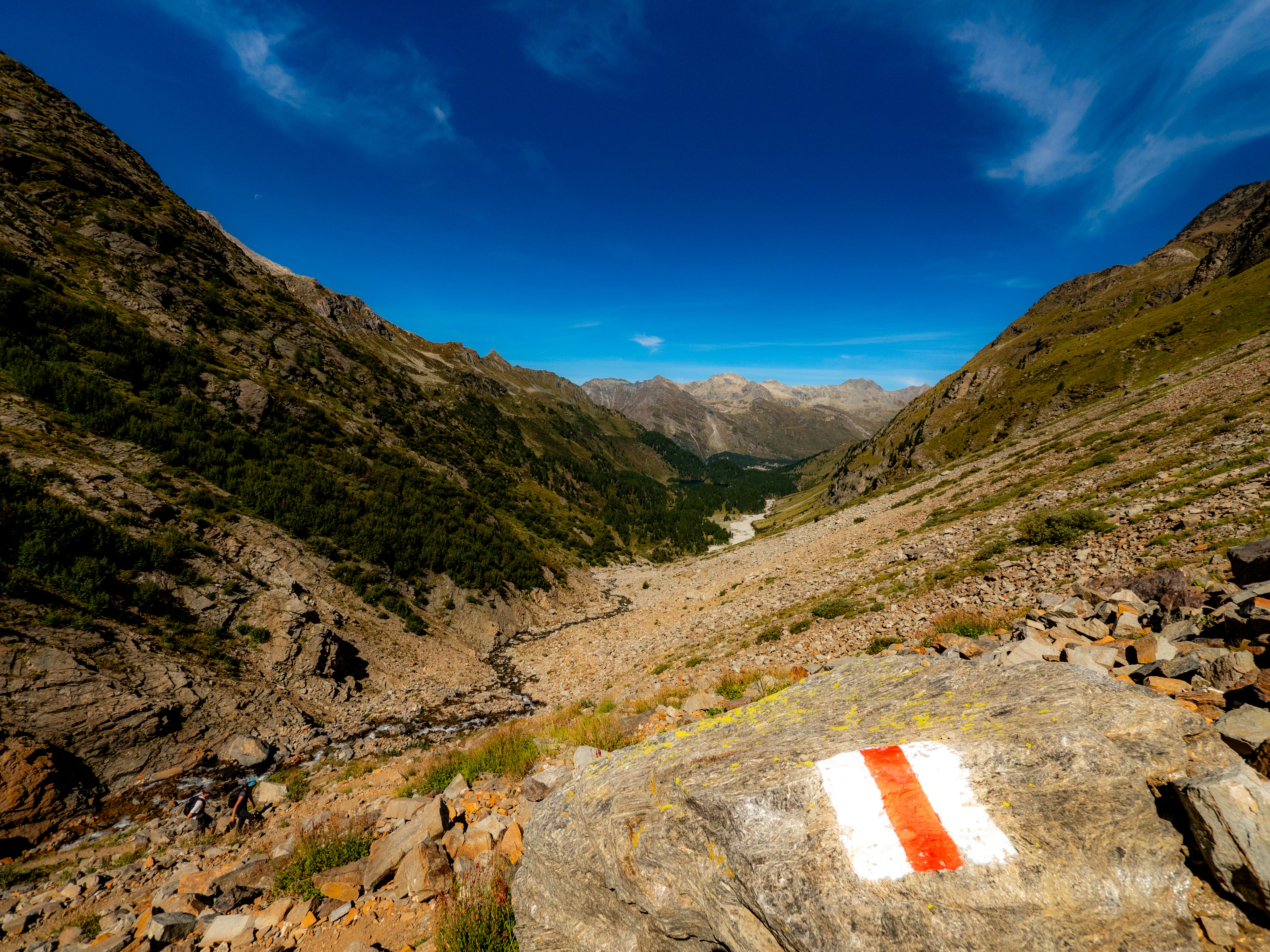 A red and white trail marker on a rock in a mountain valley