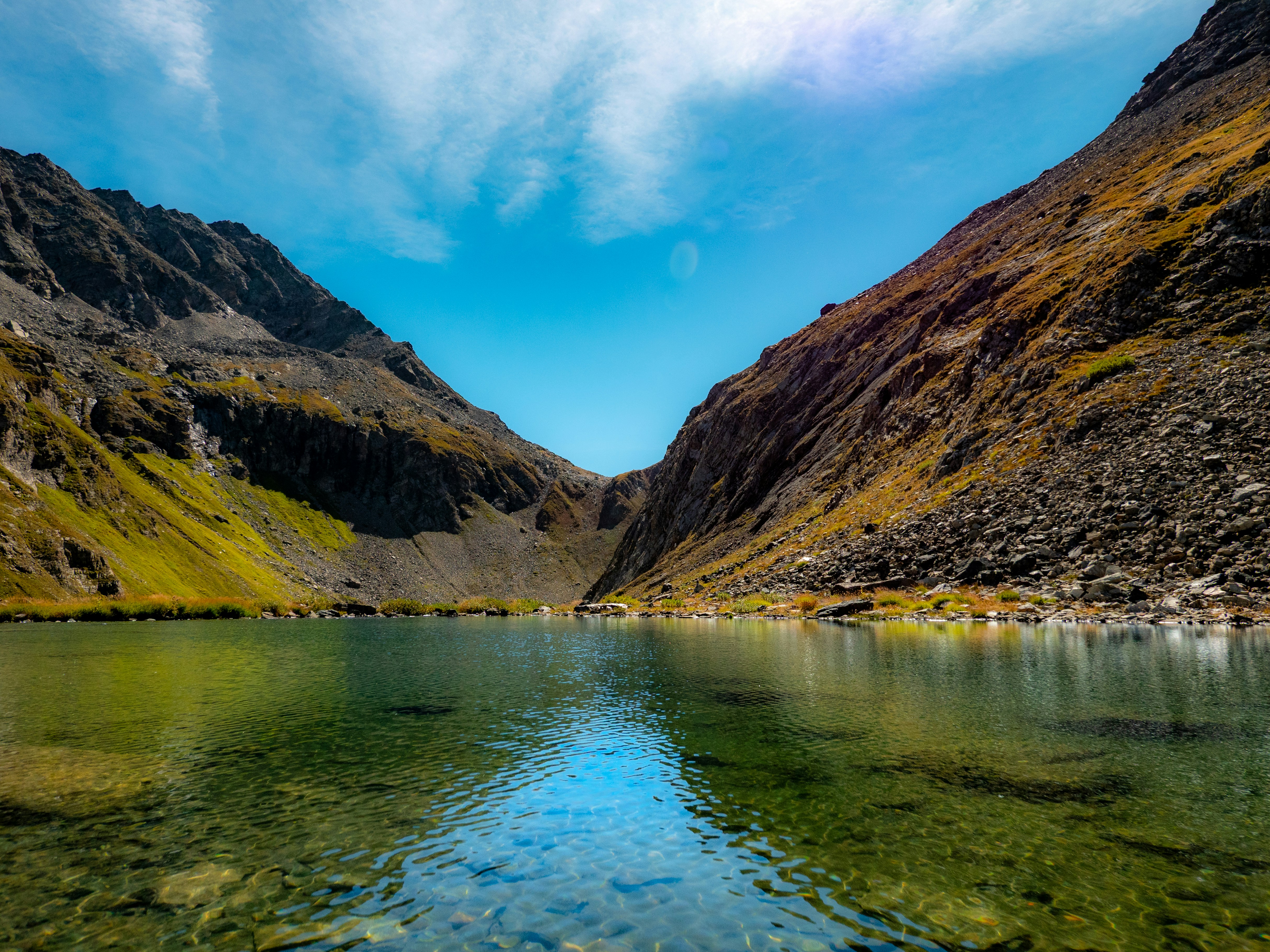 A clear alpine lake surrounded by steep rocky mountain slopes under a blue sky