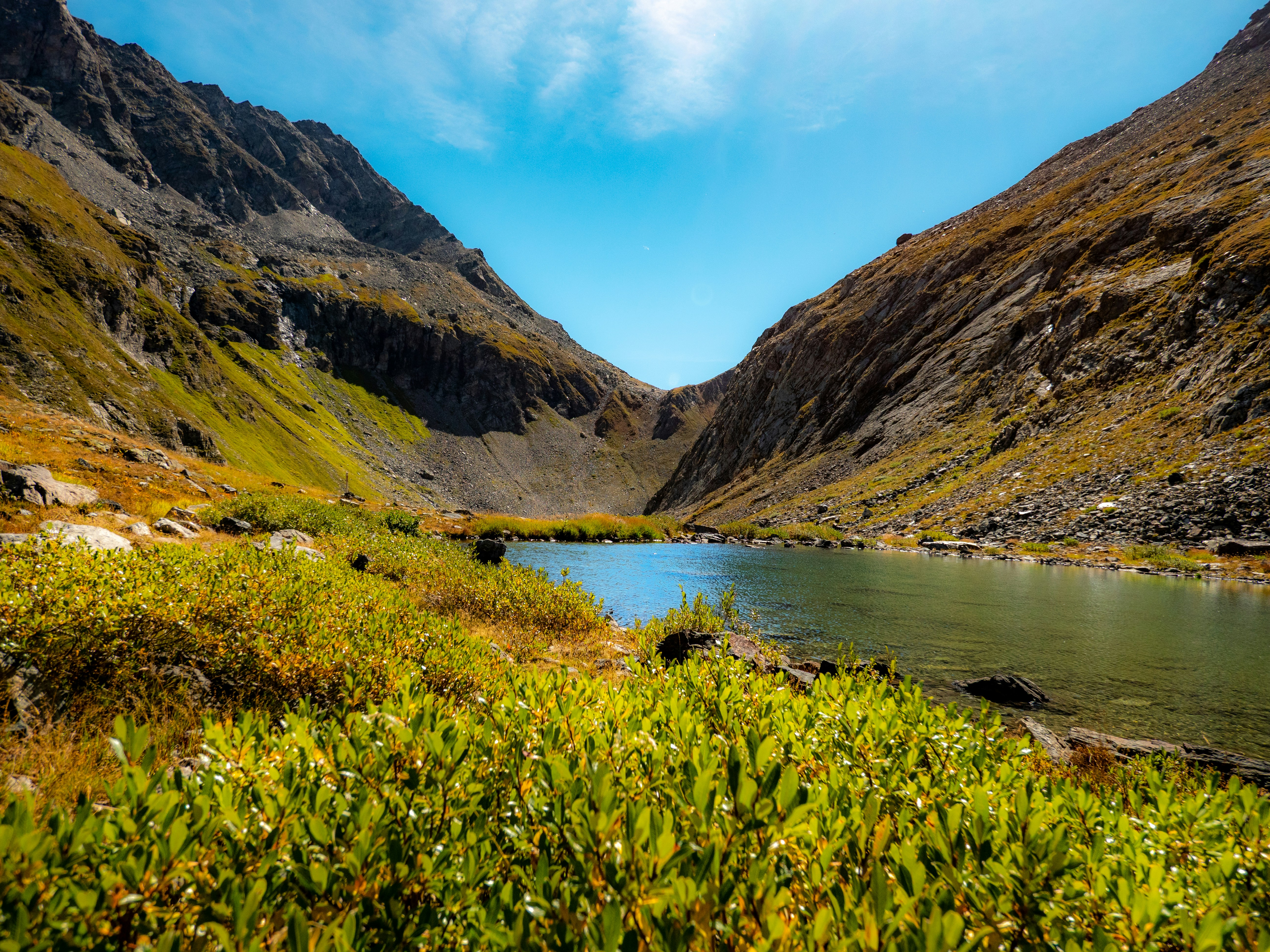 A calm alpine lake nestled between steep rocky mountain slopes under a blue sky