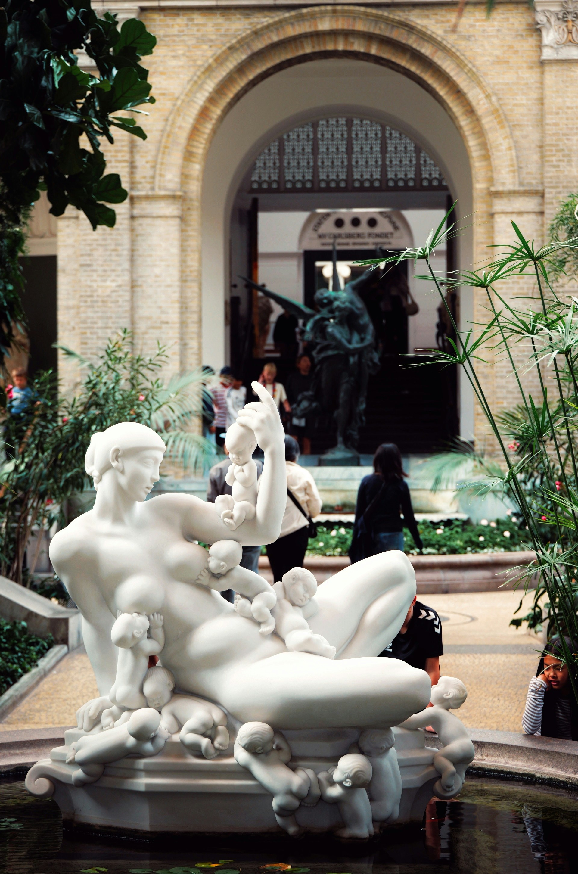 A white marble sculpture of a woman surrounded by many small infants