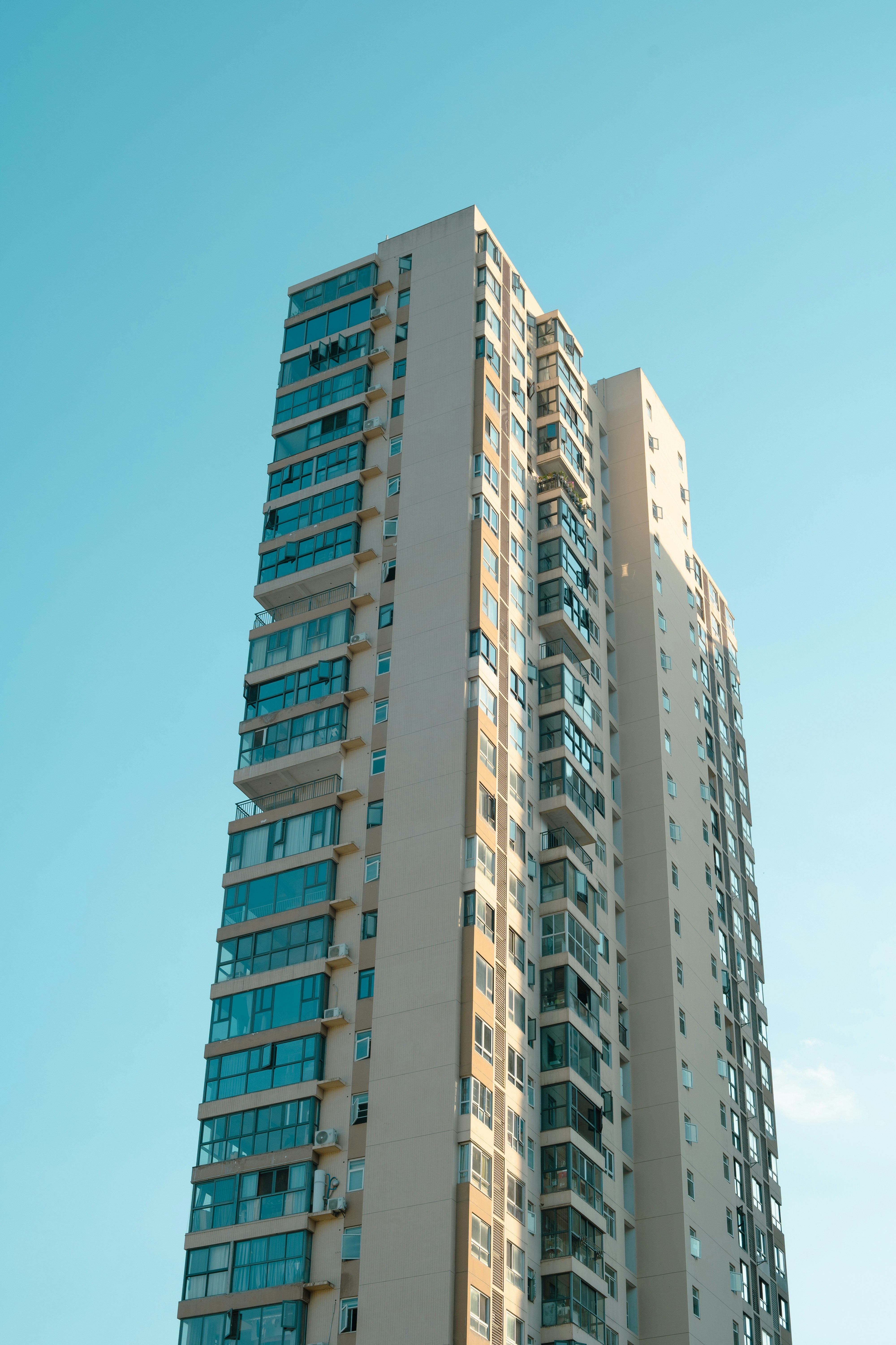 Ein hohes Wohnhaus mit Glasbalkonen vor klarem blauen Himmel