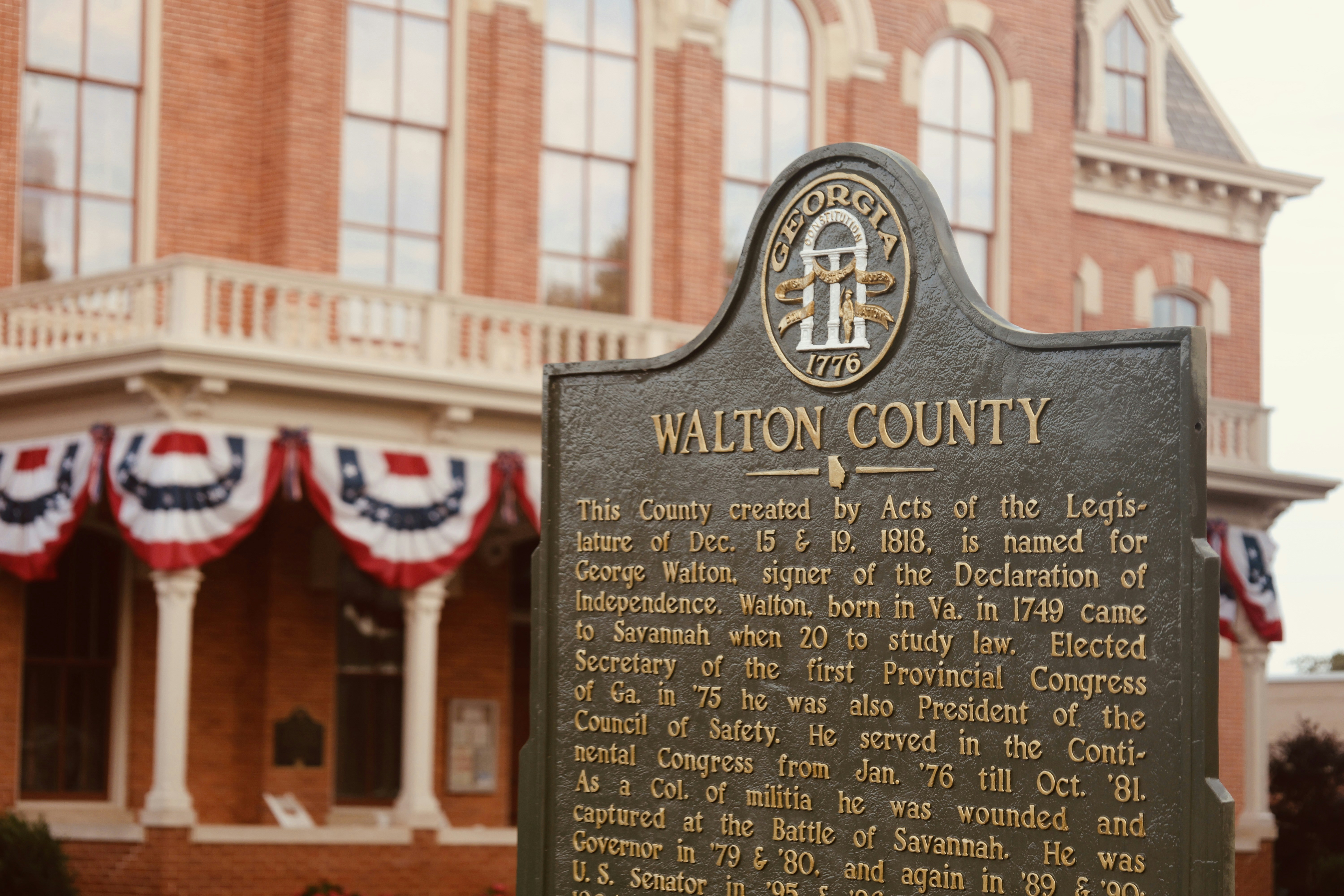 A Walton County historical marker in front of a brick building with patriotic bunting - roadside historical markers