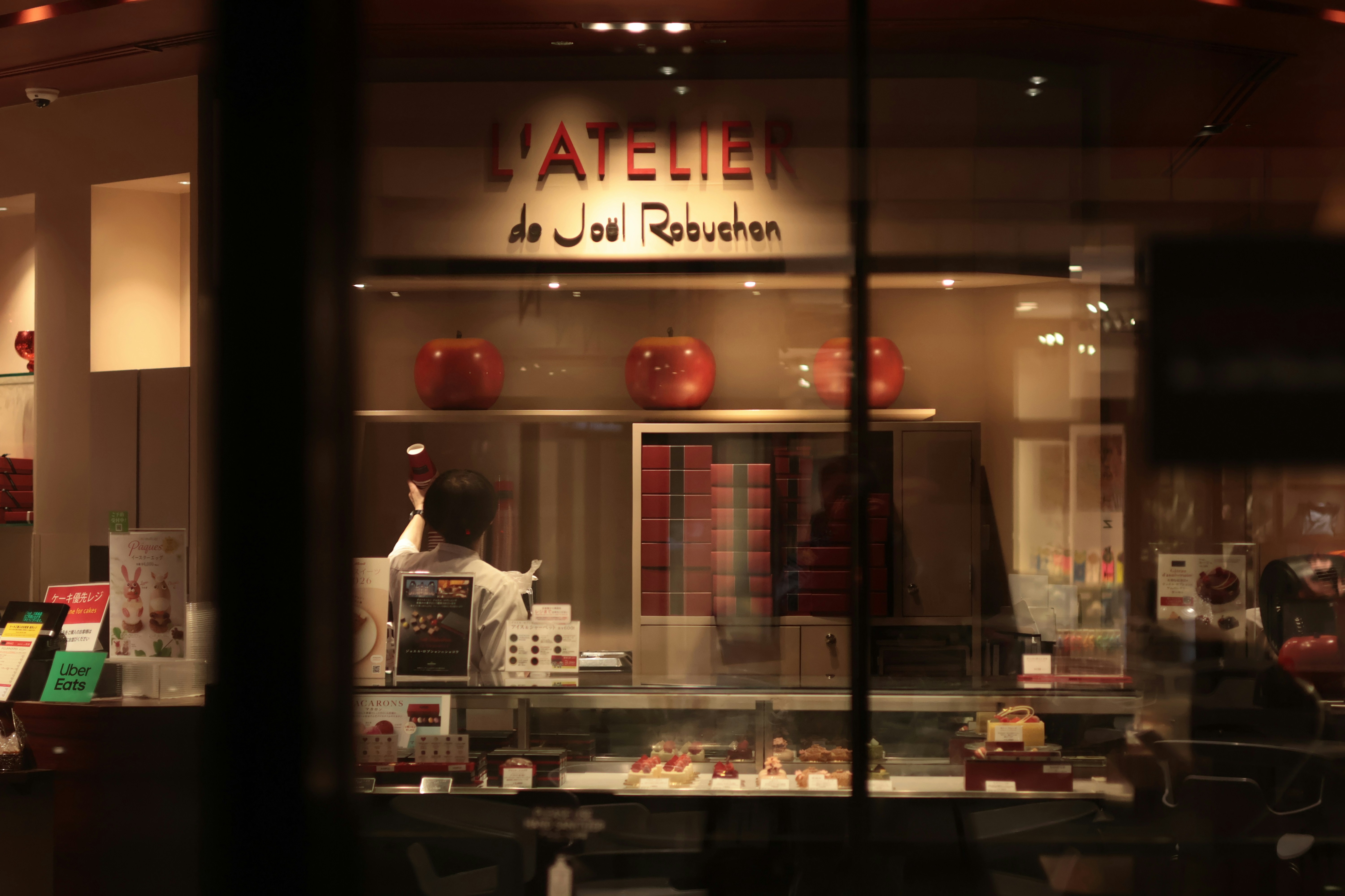 A person working behind the counter of a patisserie with red apple decorations
