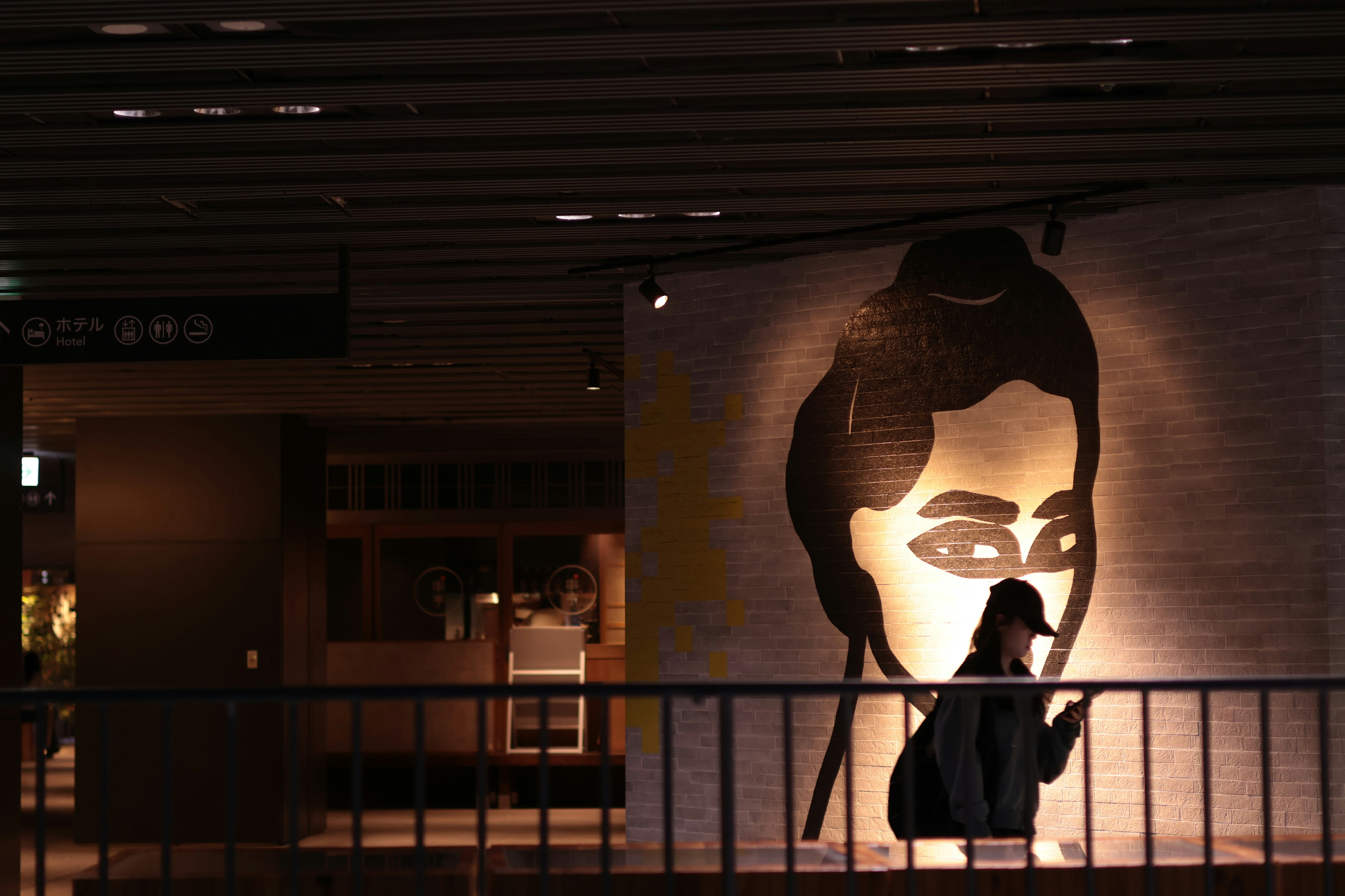 A person in a cap walking past a large mural of a face