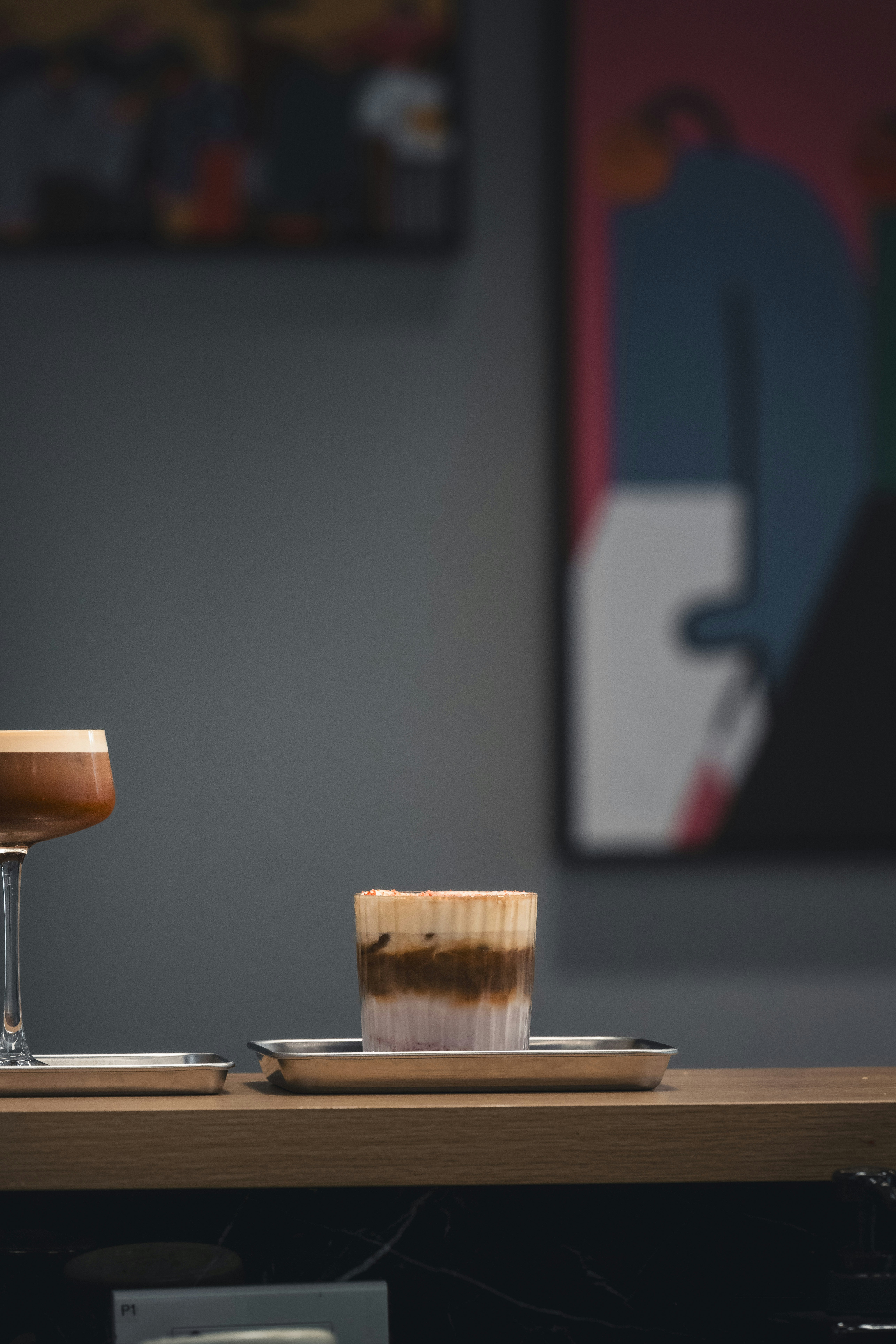 A layered coffee drink in a glass on a metal tray on a counter