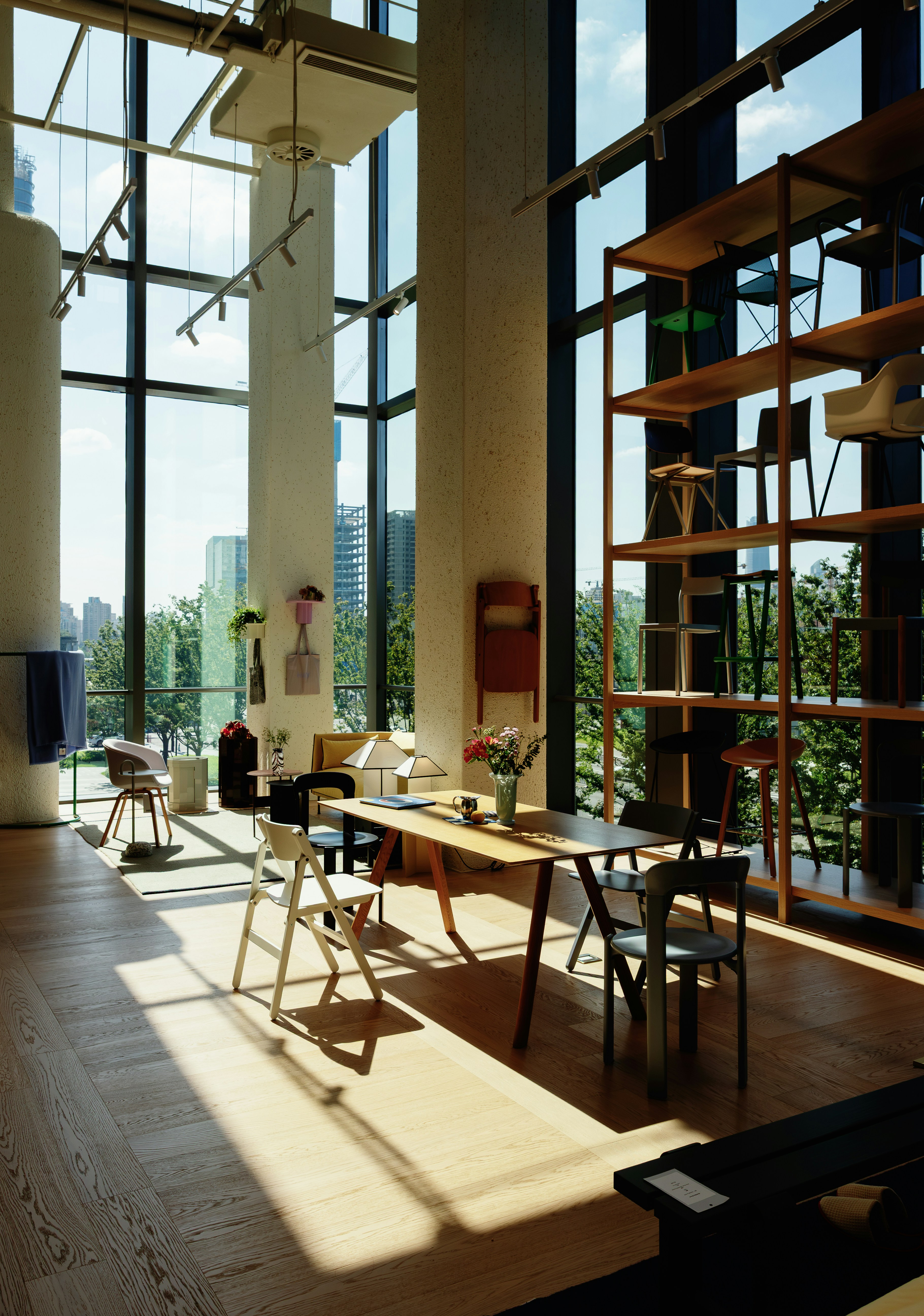 A bright showroom with oak tables and chairs beside tall windows over the city