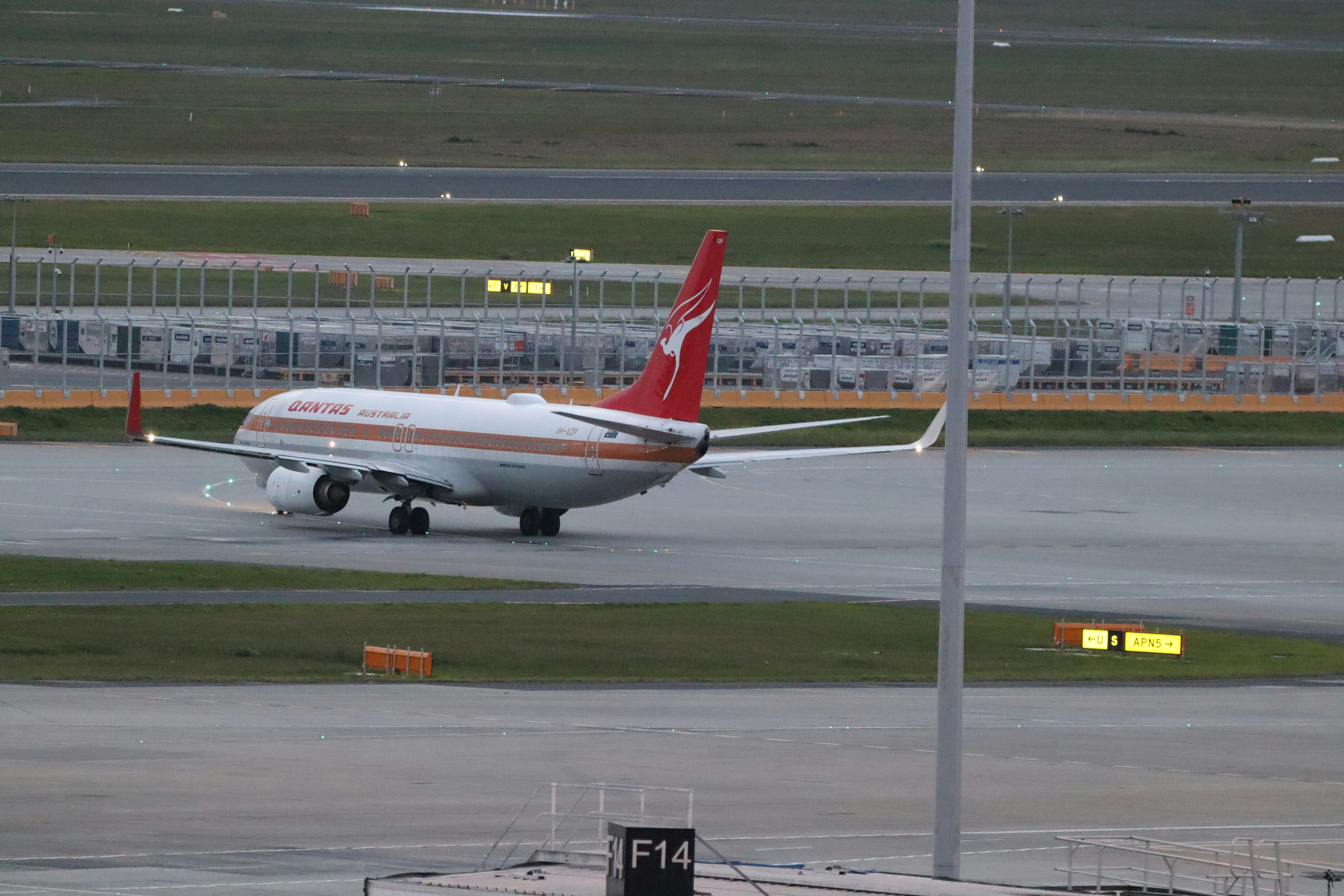 A Qantas passenger jet taxiing on an airport runway at dusk