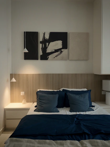 A bed with dark blue bedding and pillows against a wooden headboard wall