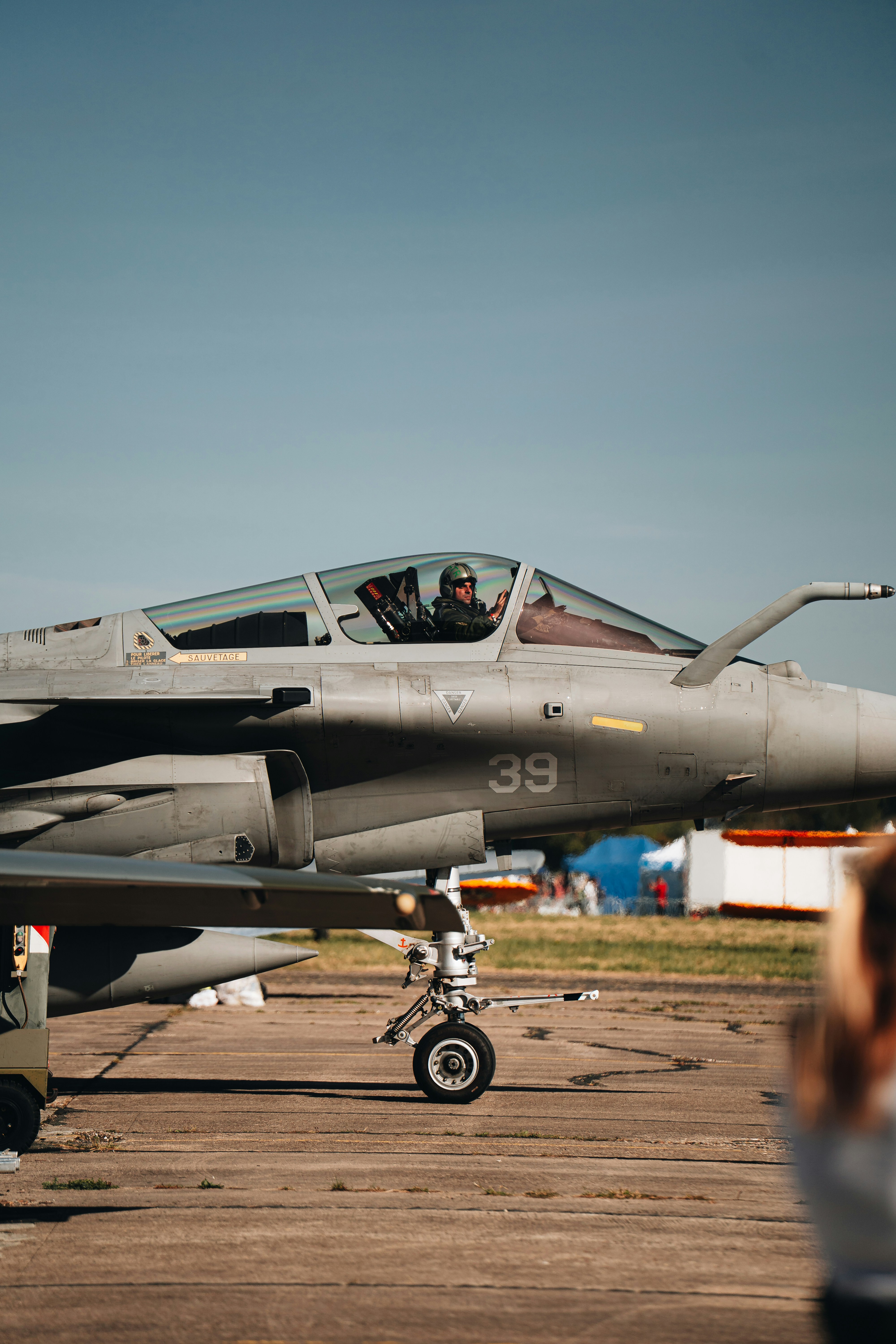 Ein Pilot im Cockpit eines grauen Kampfjets auf einem Flugplatz