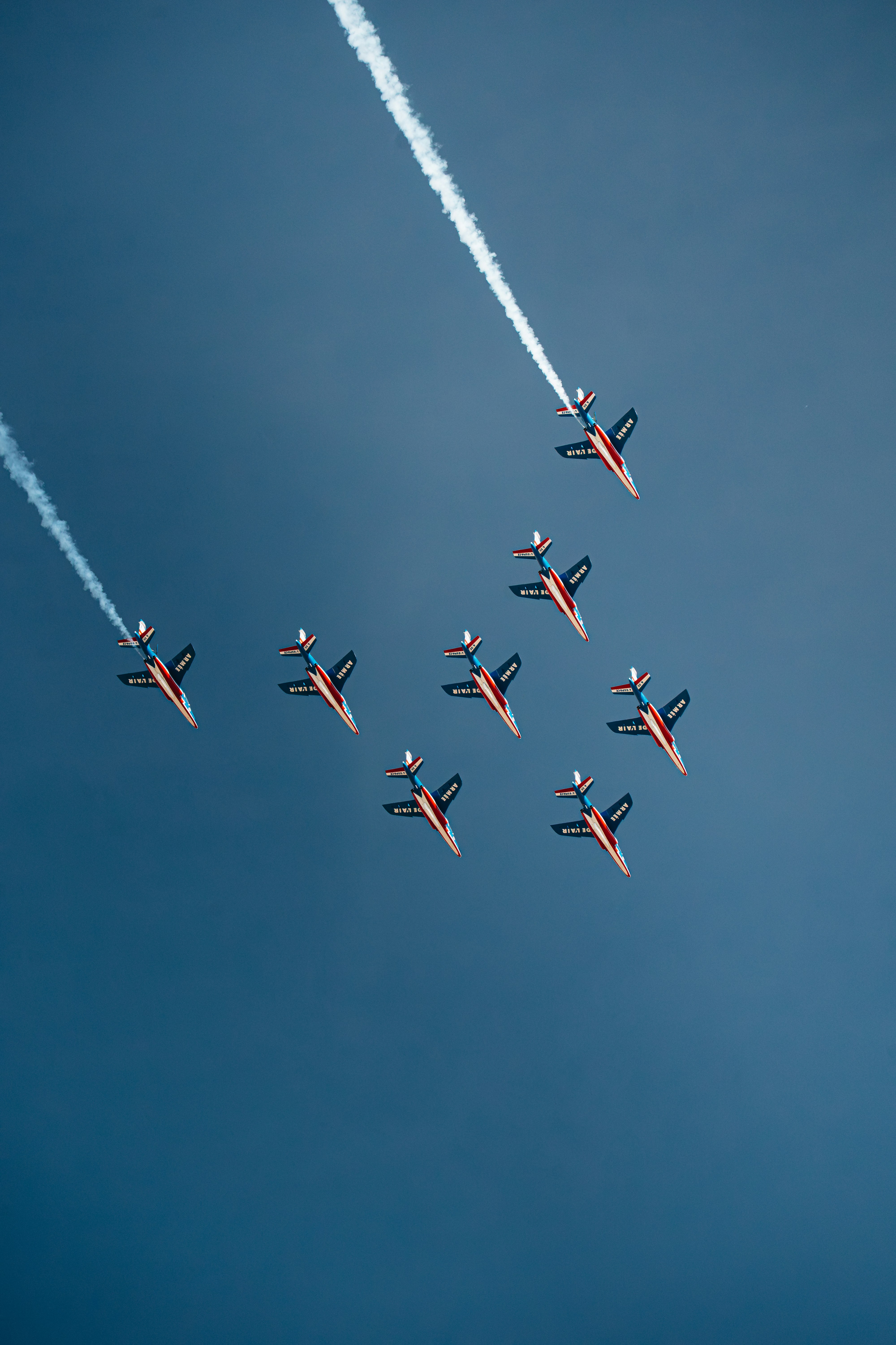 Acht Kampfjets fliegen in Formation gegen einen klarblauen Himmel mit Rauchspuren