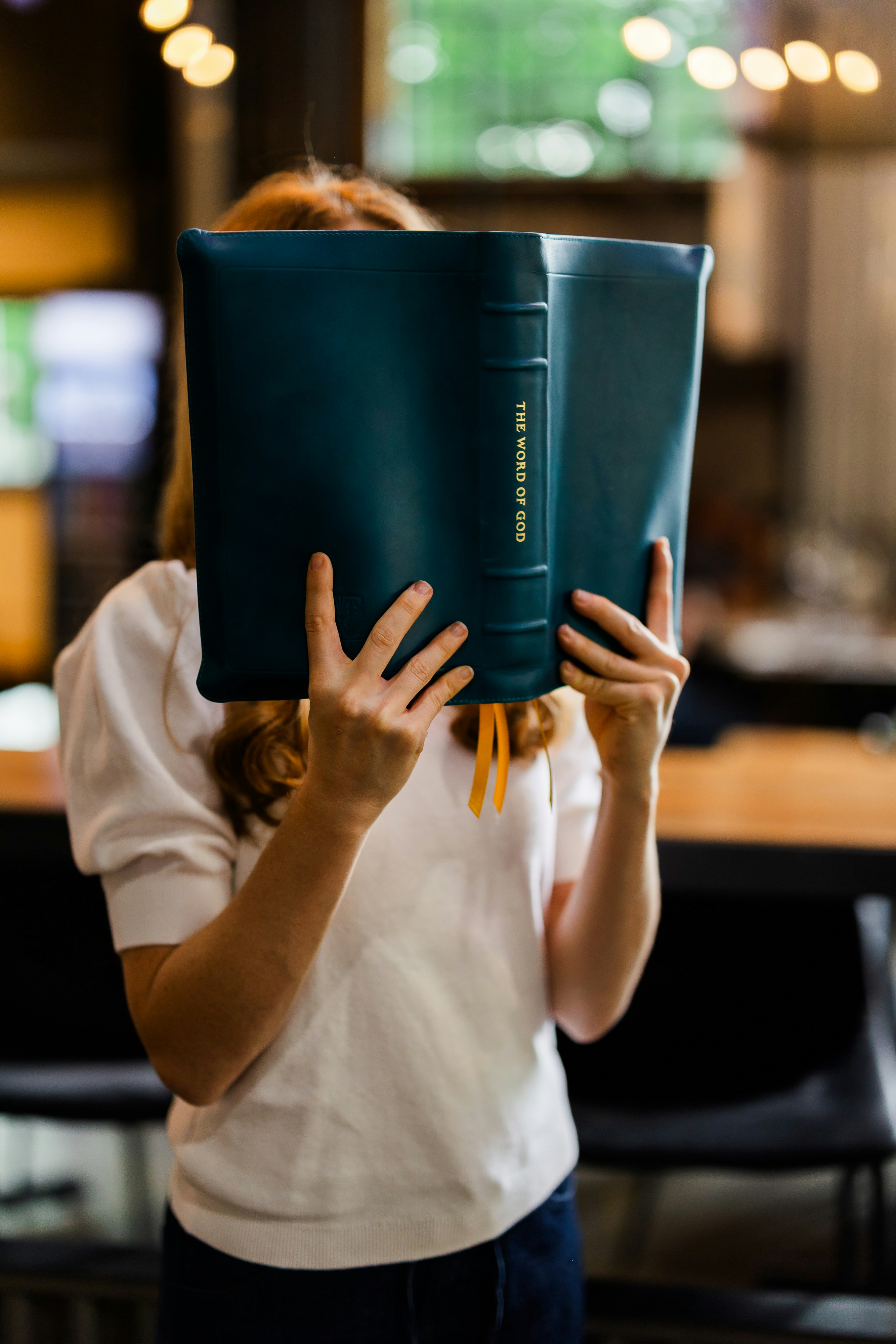 Una donna che tiene un libro color turchese con scritto "LA PAROLA DI DIO" sul volto