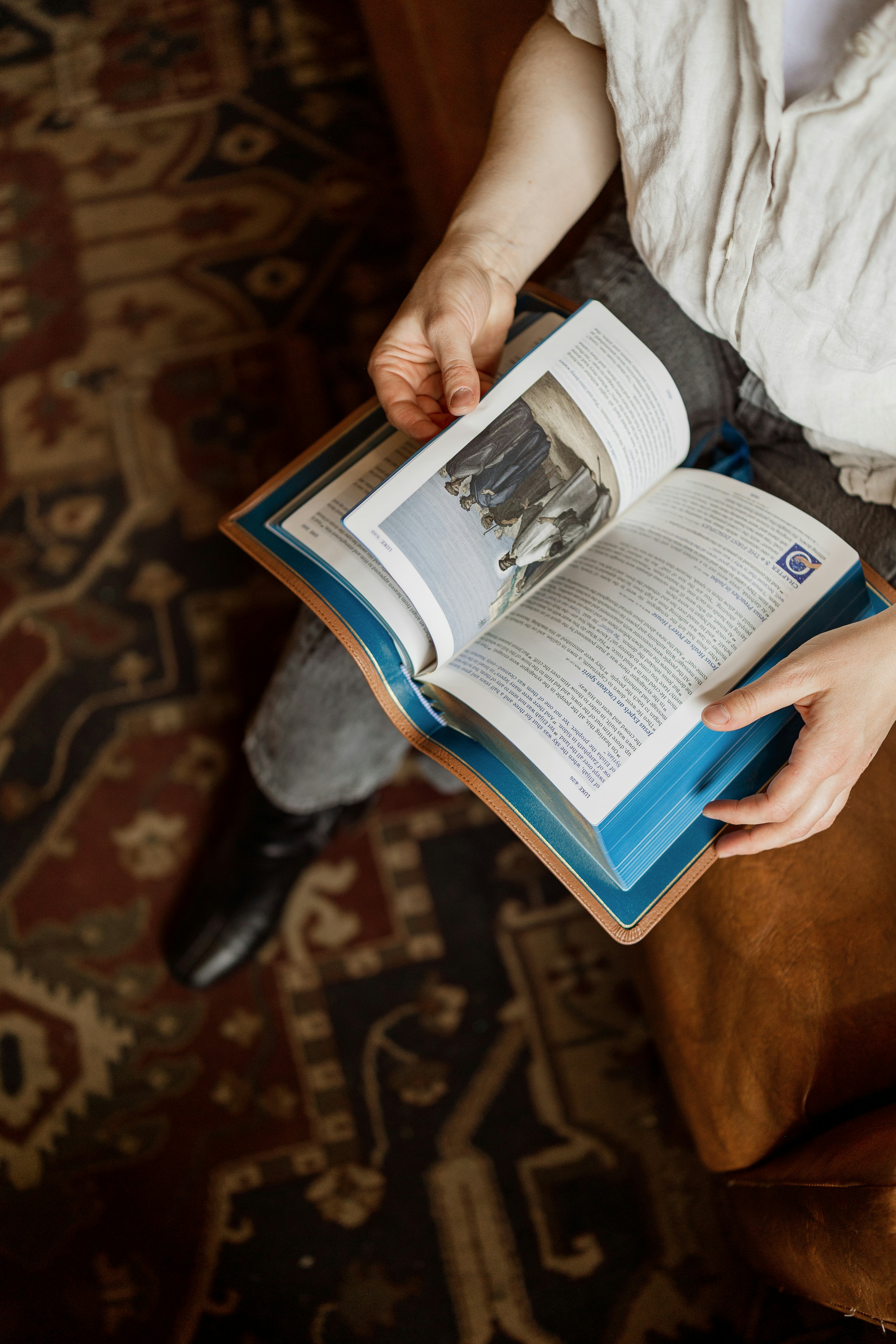 Una persona con una camicia bianca che legge un libro illustrato aperto sulle ginocchia