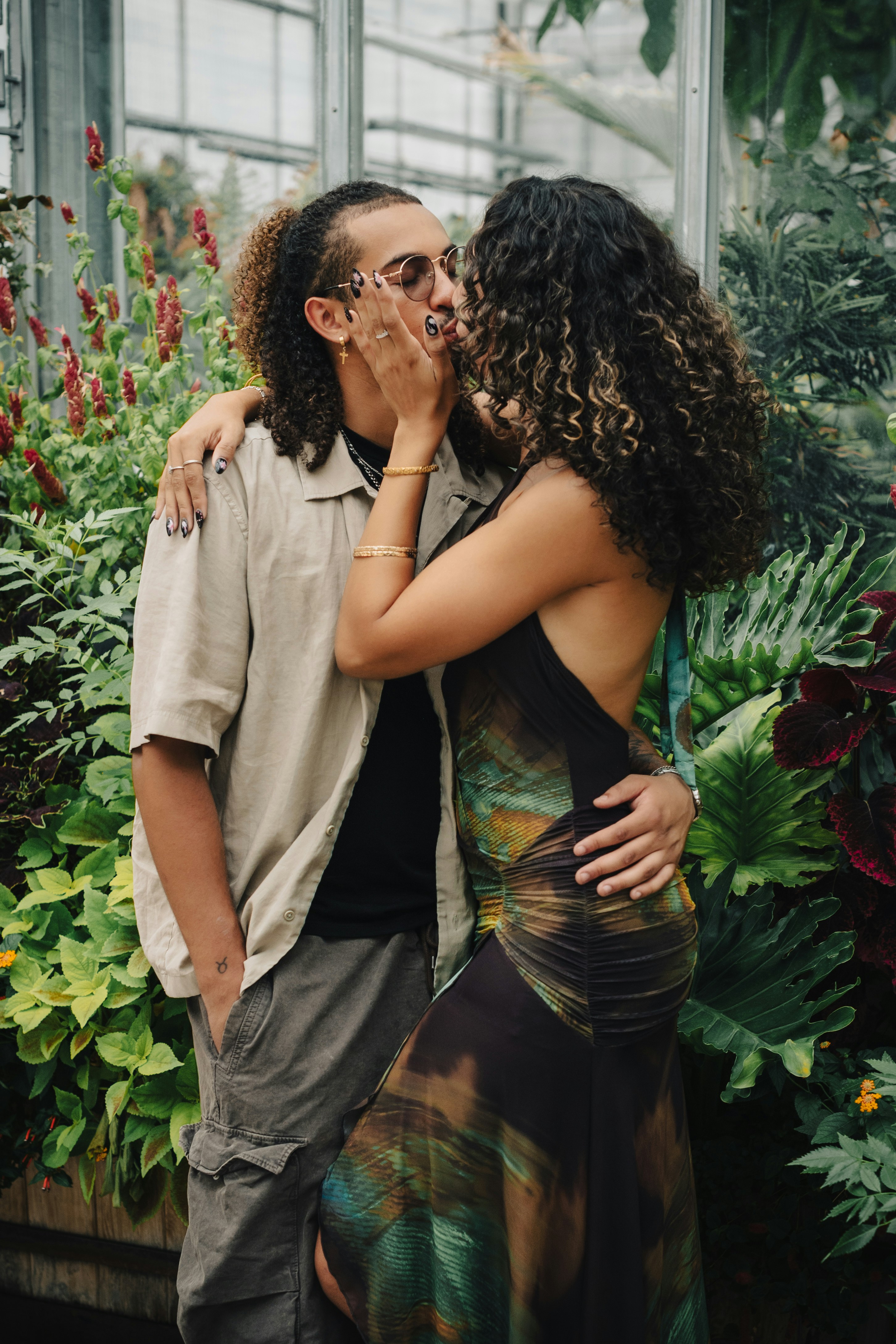 A man and a woman kissing among lush green plants in a greenhouse