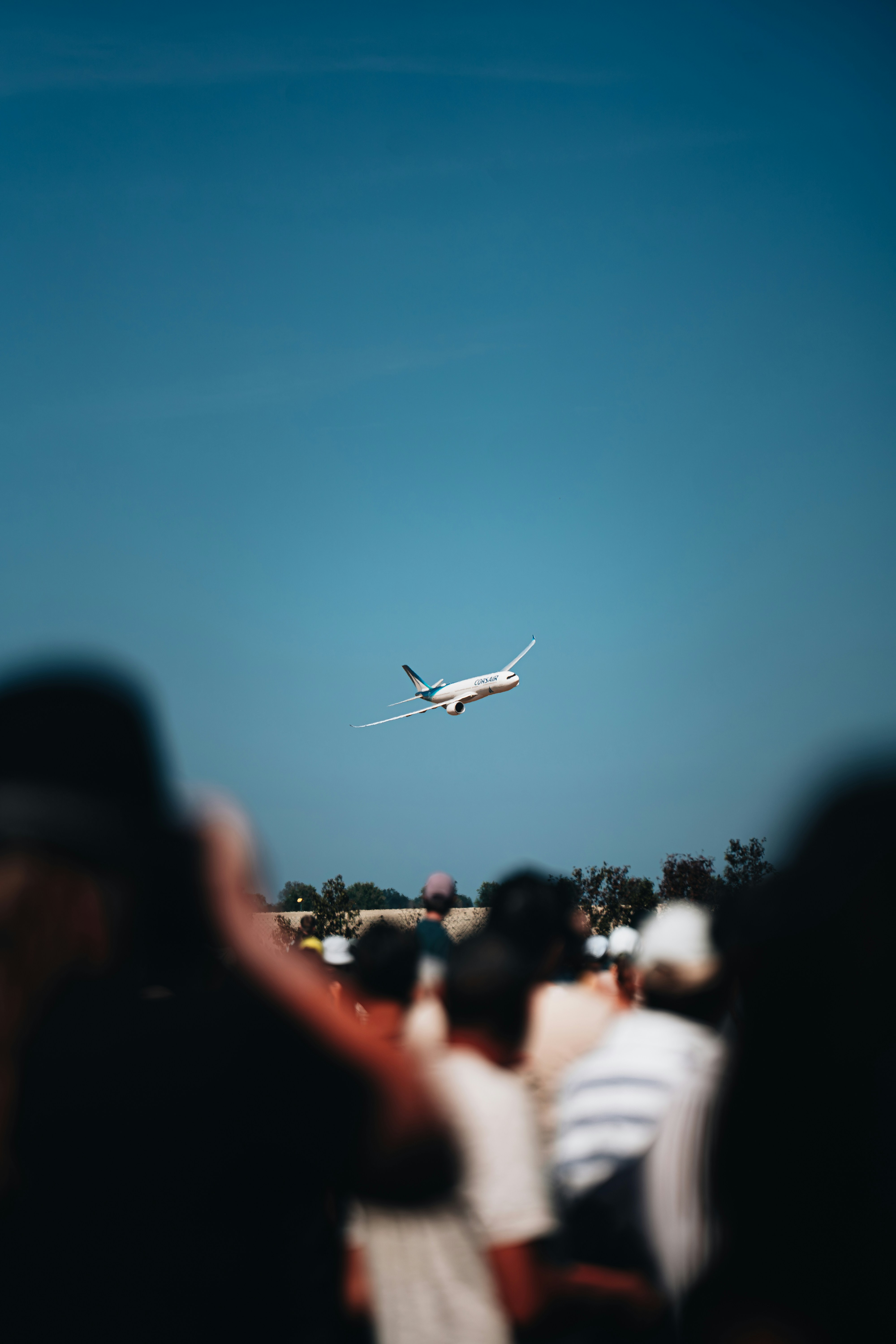 Ein Passagierflugzeug fliegt an einem klaren blauen Himmel über einer Menschenmenge