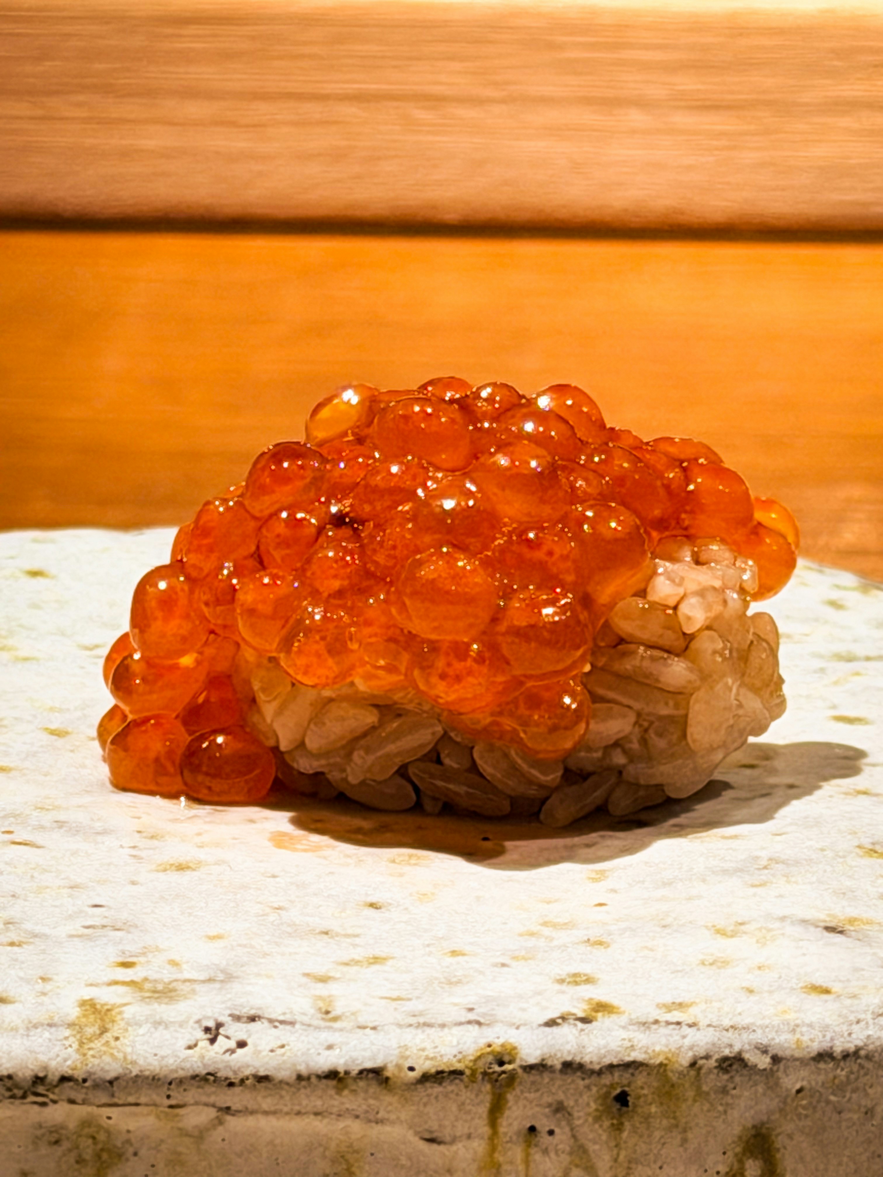 A piece of salmon roe sushi on a textured stone plate
